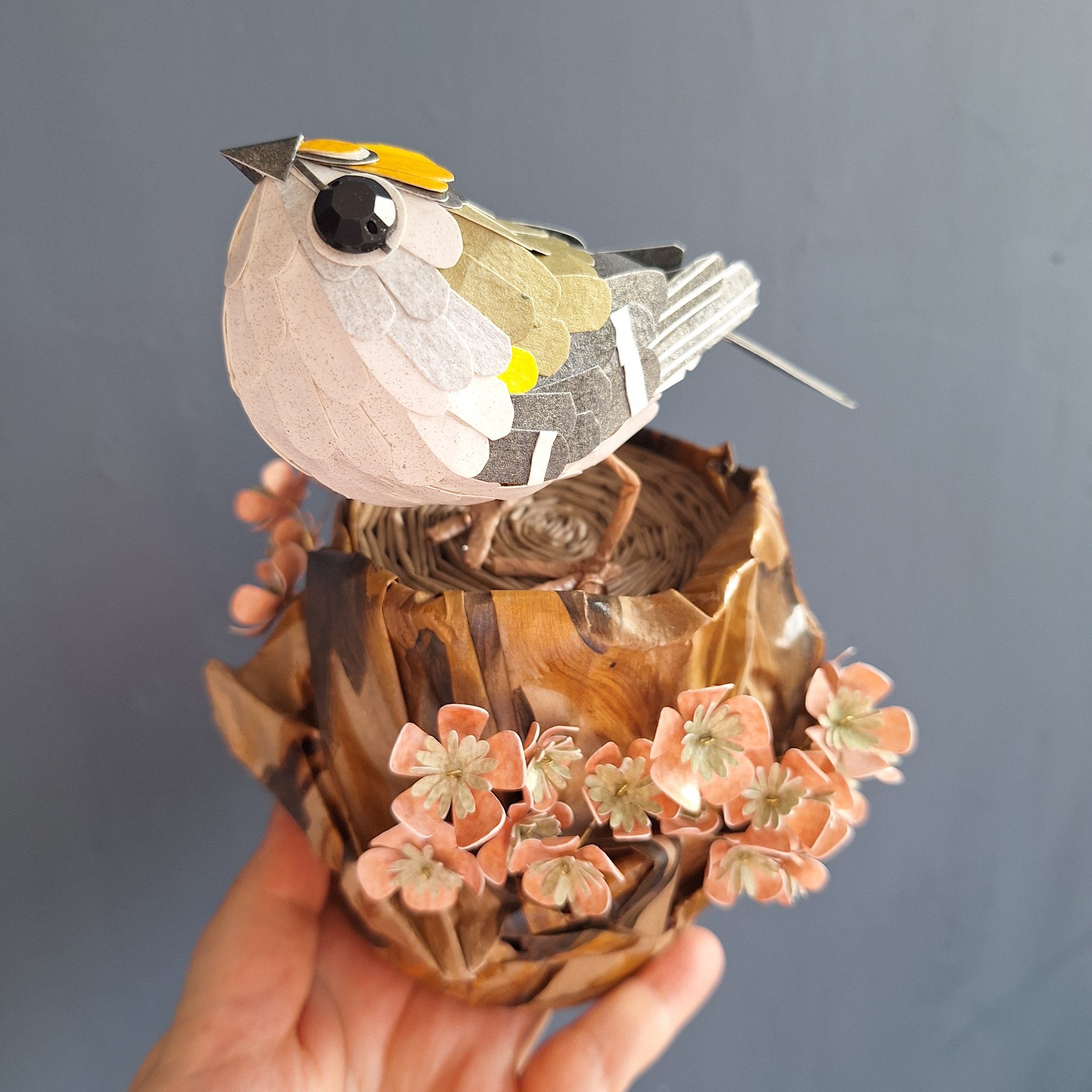 close up of a handmade goldcrest bird sculpture, made from recycled and hand printed papers