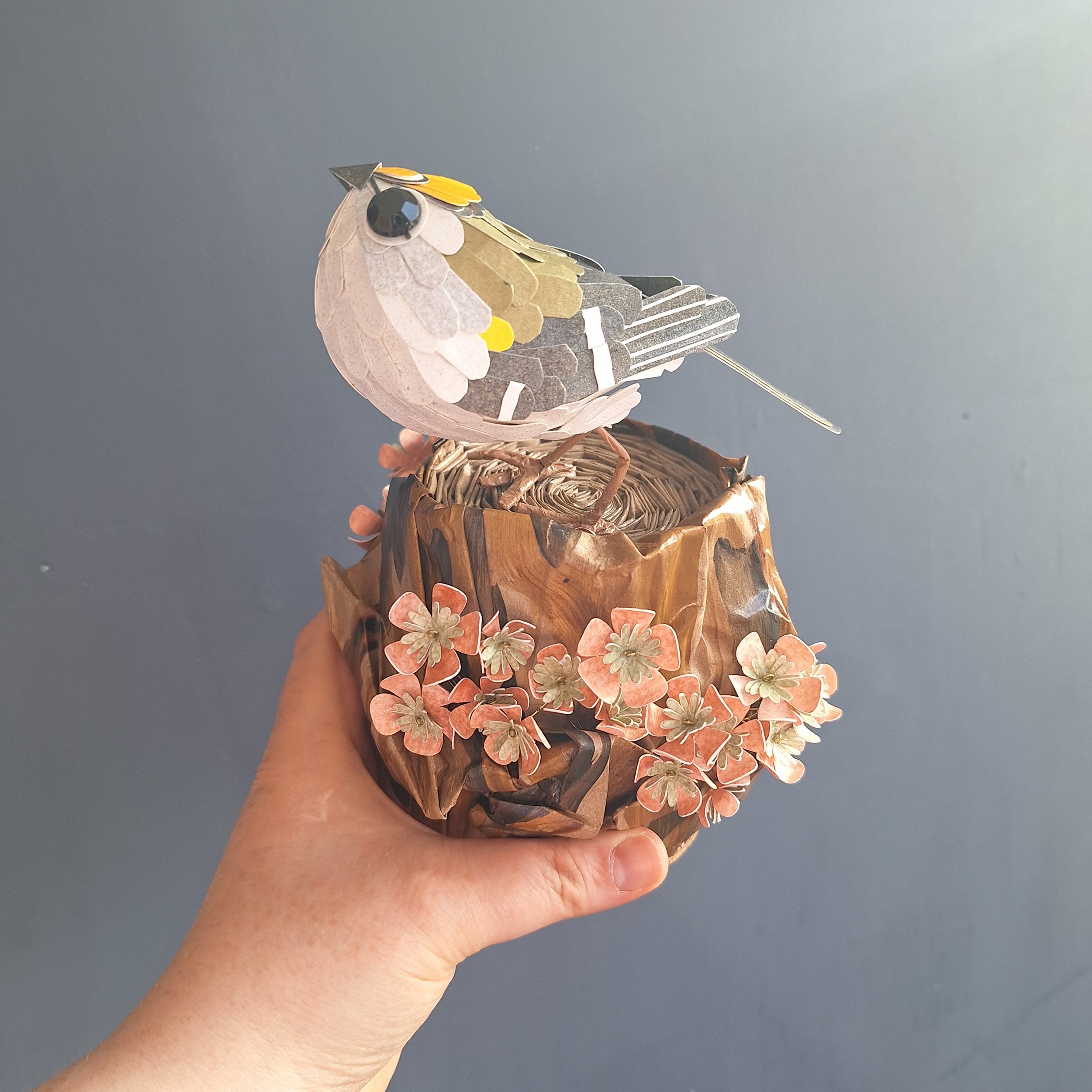 side view of a paper sculpture of a small garden bird, perched on a tree stump