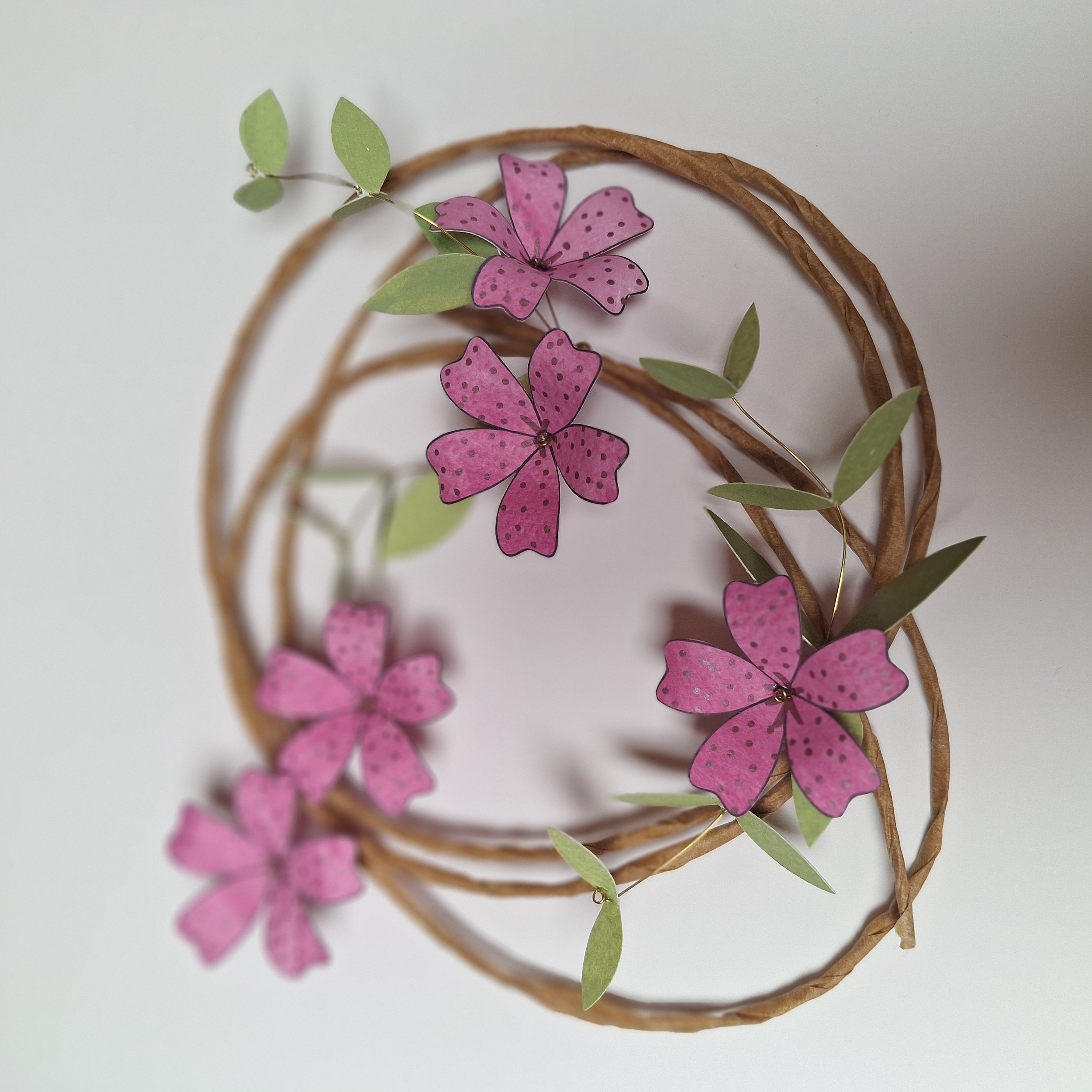 This flower wreath has five bright pink flowers, accompanied red by leafy stems. The flowers are all the same size, and they have fold spot details on their petals.