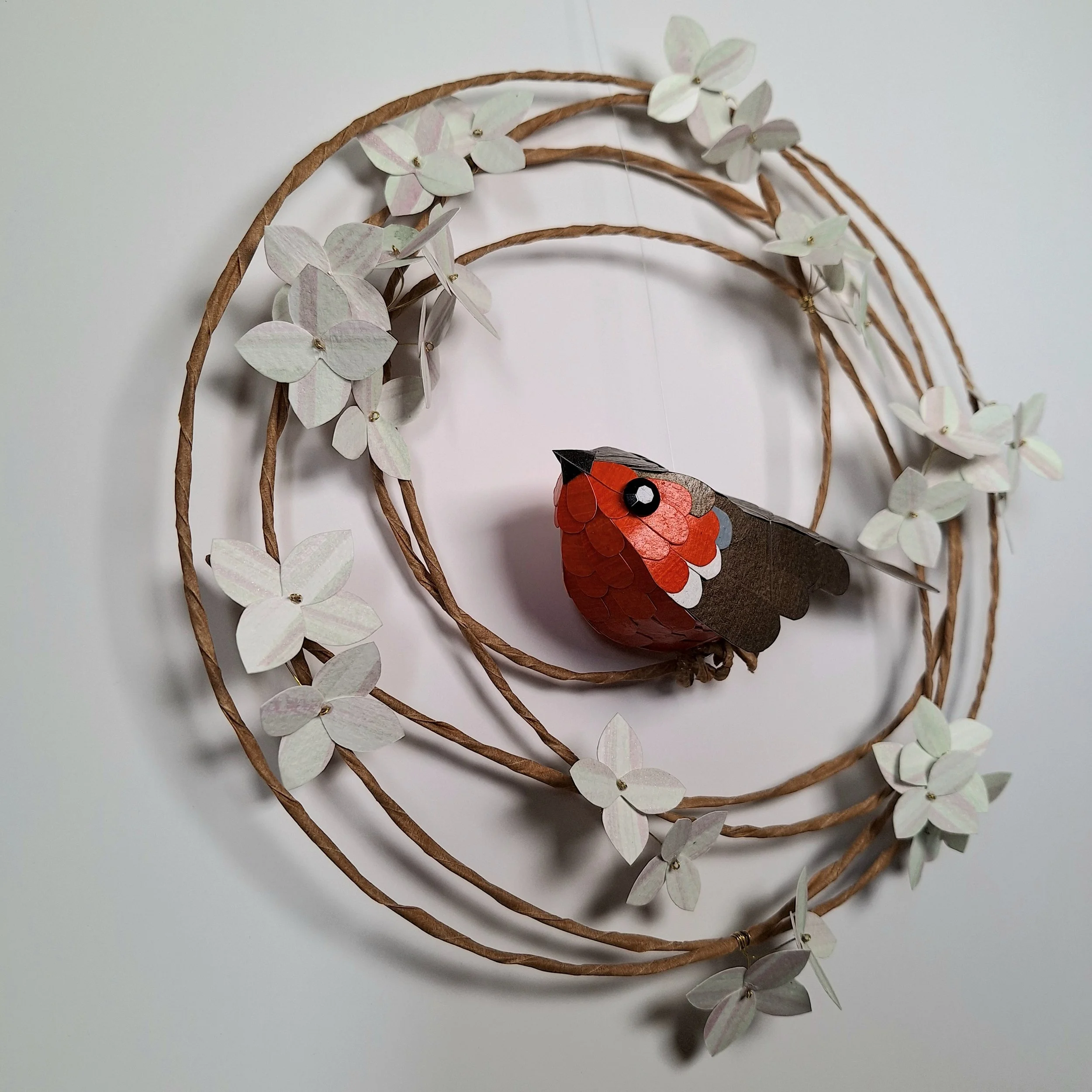 A side view of the robin on a hydrangea wreath sculpture, where you can see his red face, dark beak and eye.