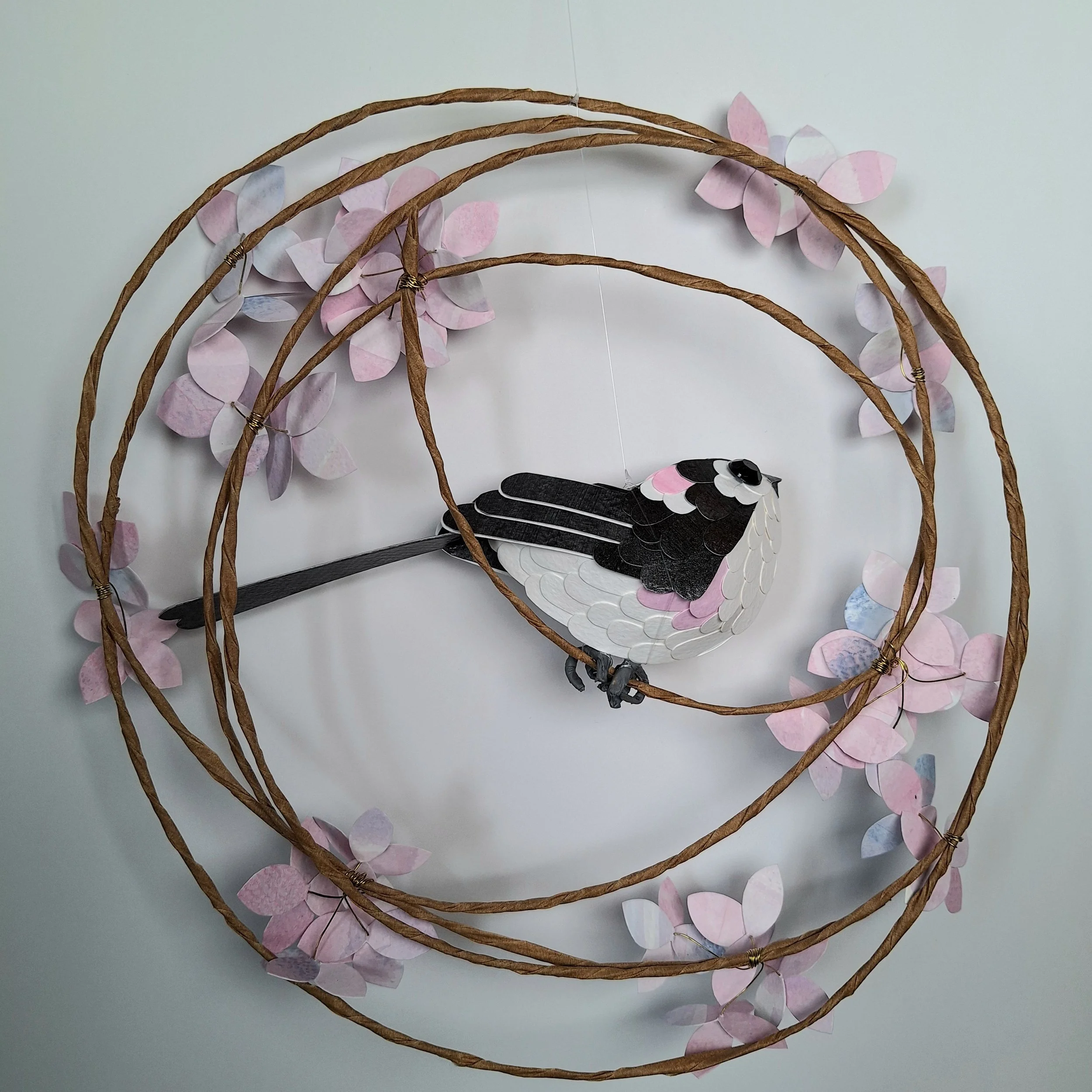 Back view of this paper sculpture wall art, depicting a long tailed tit bird, also known as a chickadee, perched on a wreath of pink hydrangea flowers.