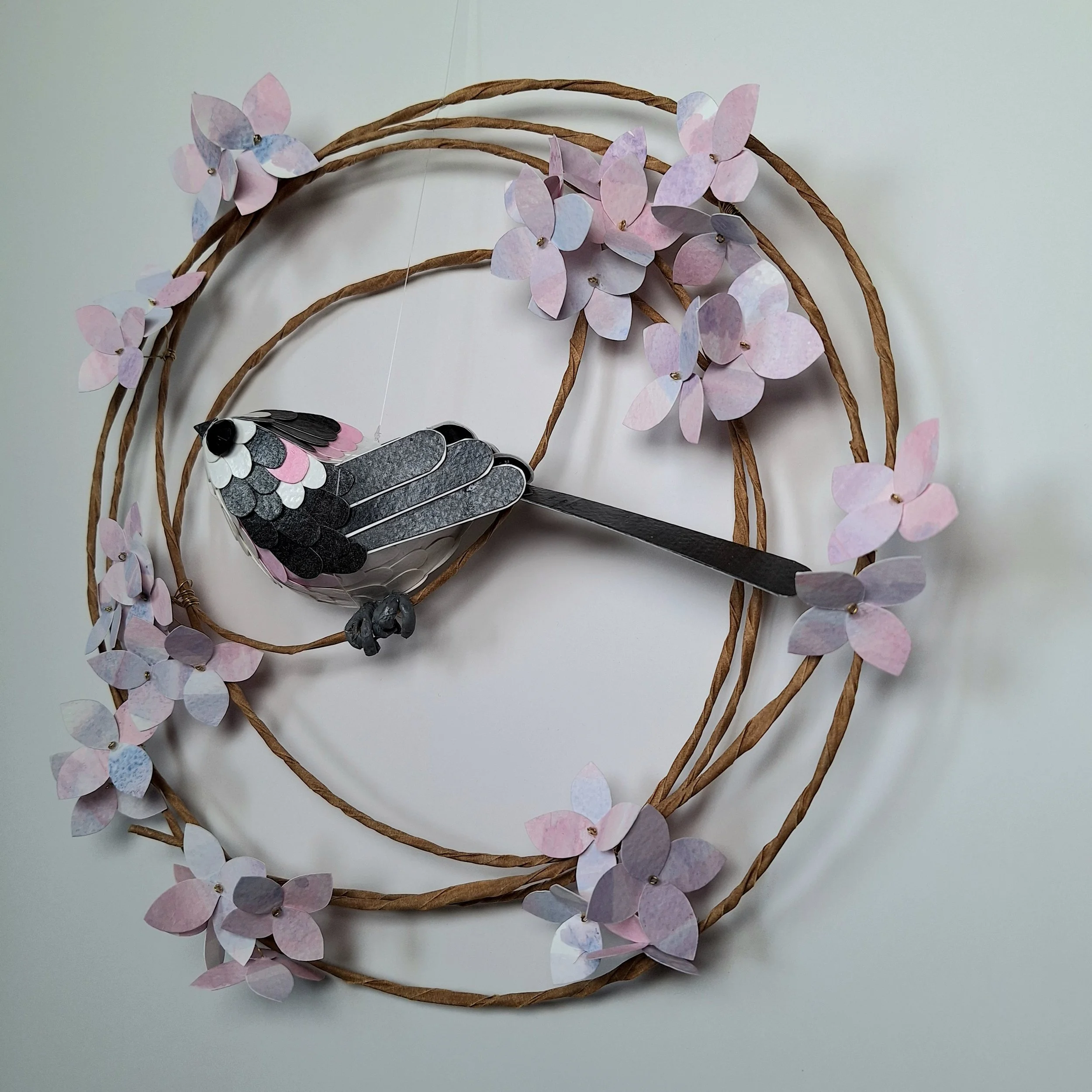 Side view of this bird wall art, The monochrome bird sculpture sits on a floral wreath of hydrangea blooms.