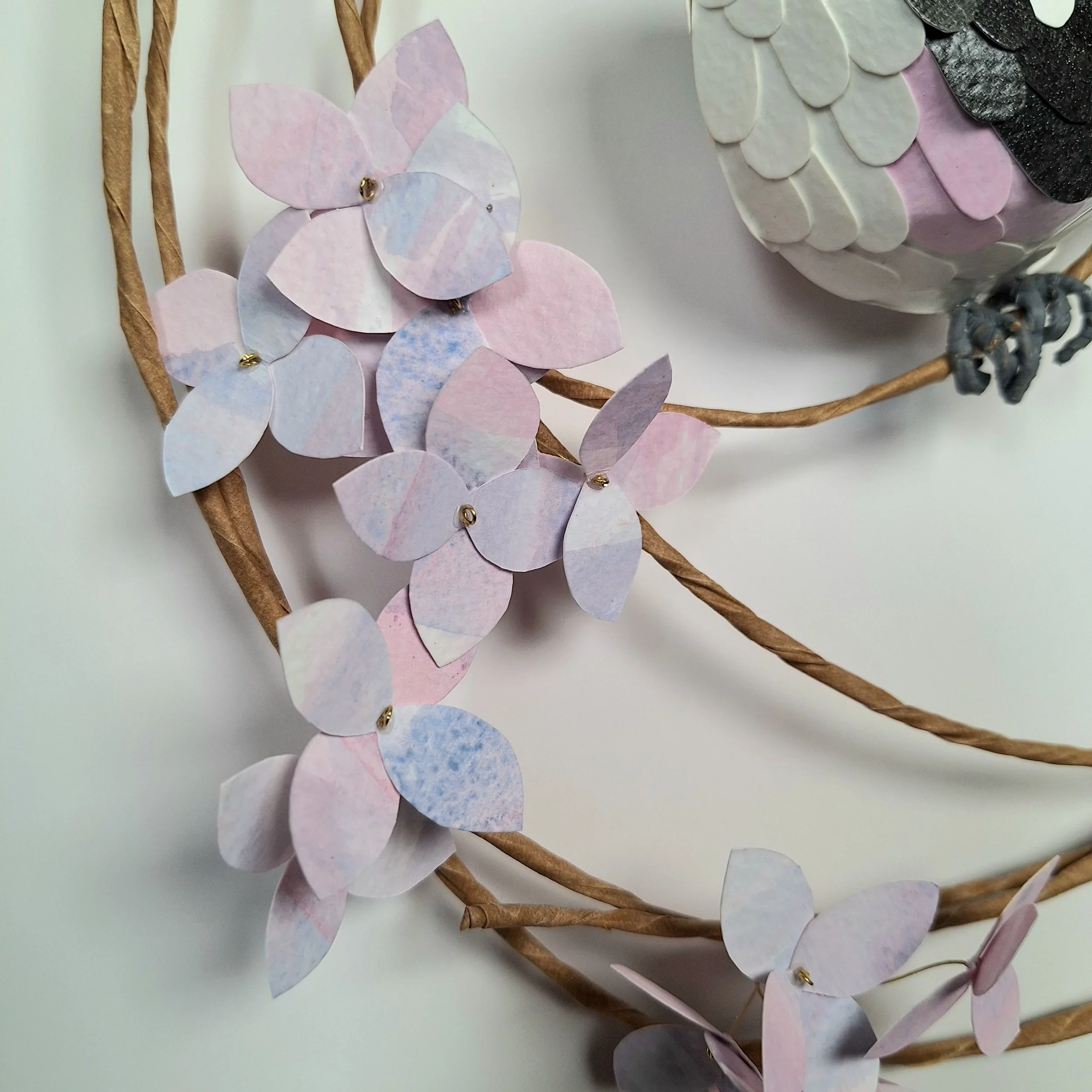 A close up of handmade paper flowers. This spring time wreath features paper hydrangea flowers in mottled pink, purple and blue. These flowers are handmade from hand-printed papers.