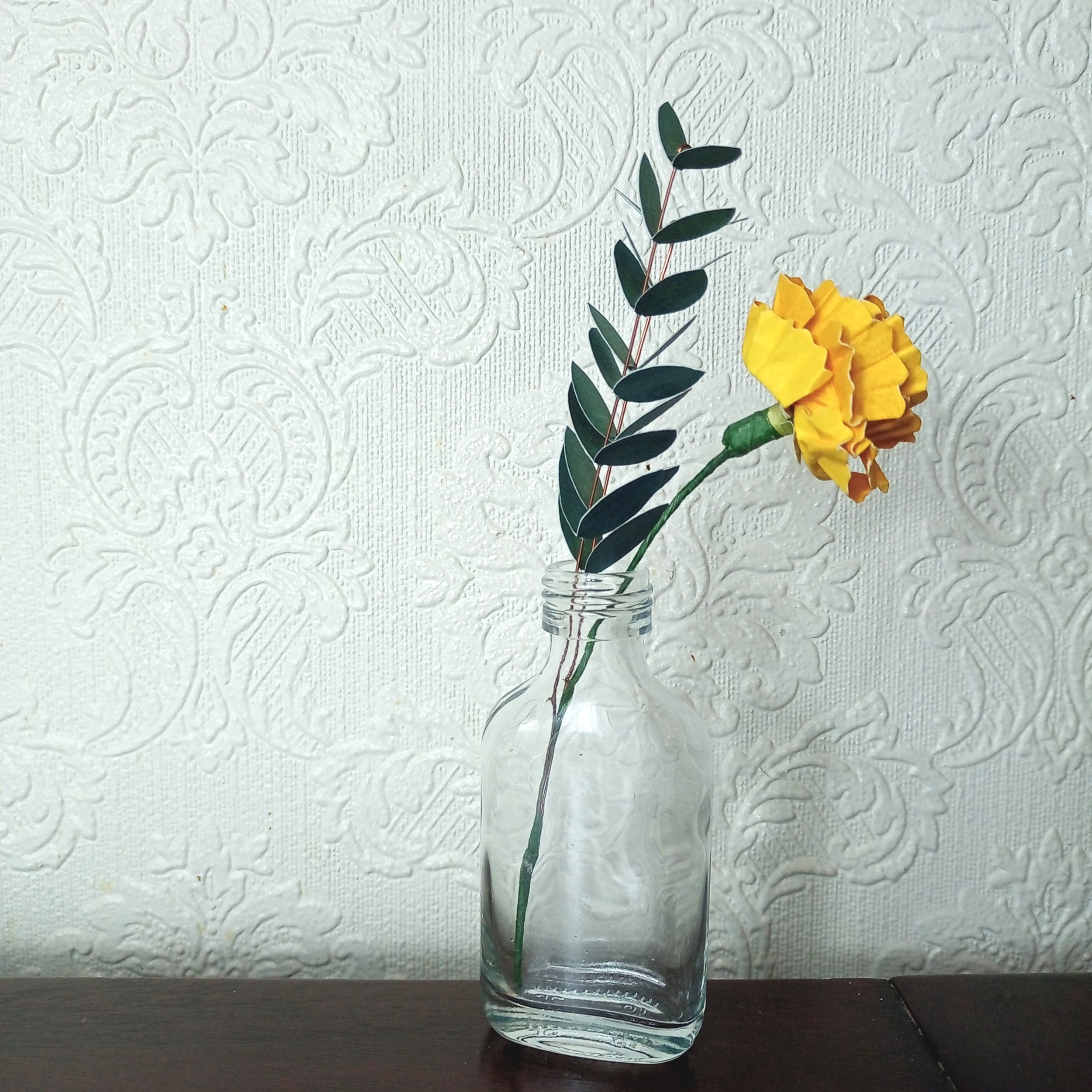 bespoke paper sculpture of a carnation flower and leafy stems in a glass bottle vase