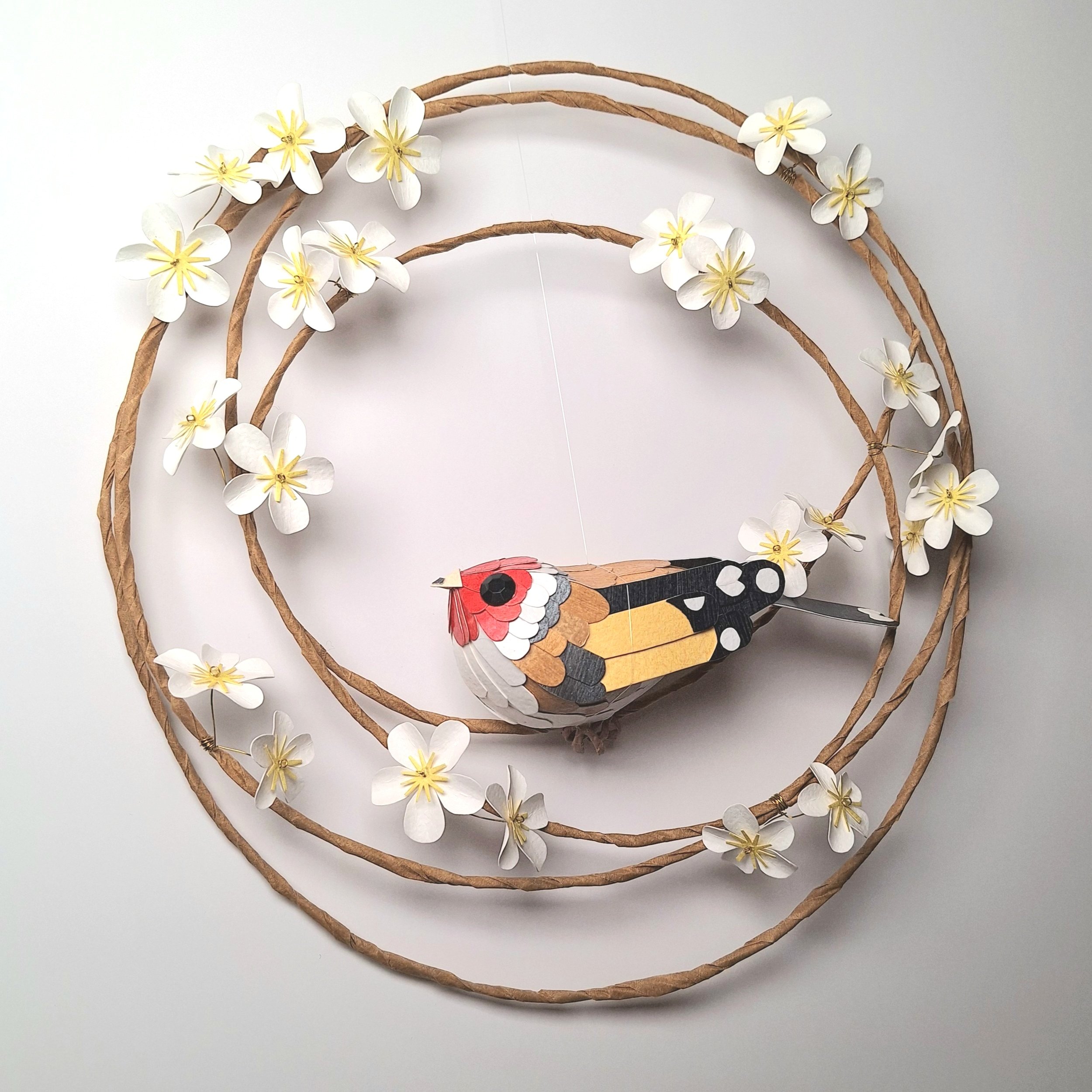 Handmade garden bird décor, featuring a paper sculpture of a goldfinch perched on a wreath of white tree blossom