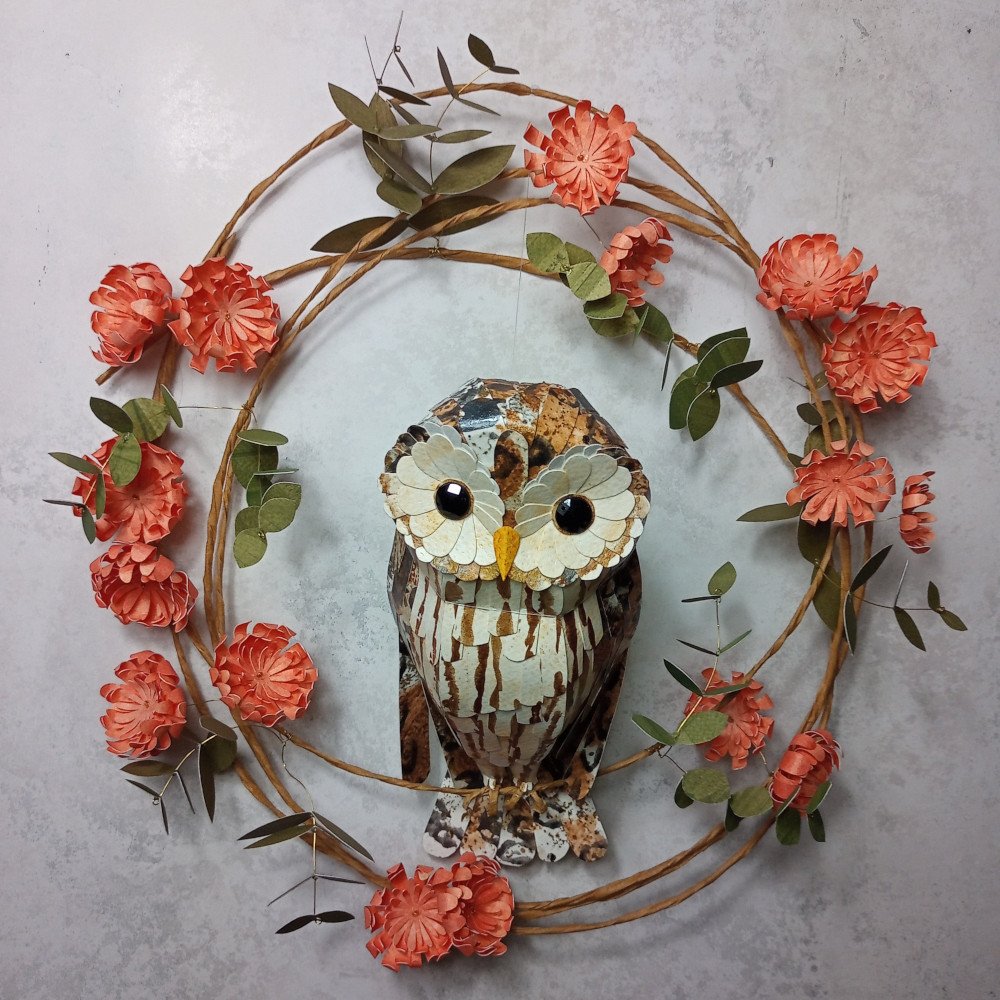 Decorative owl wreath with orange flowers and green leaves on a gray background.
