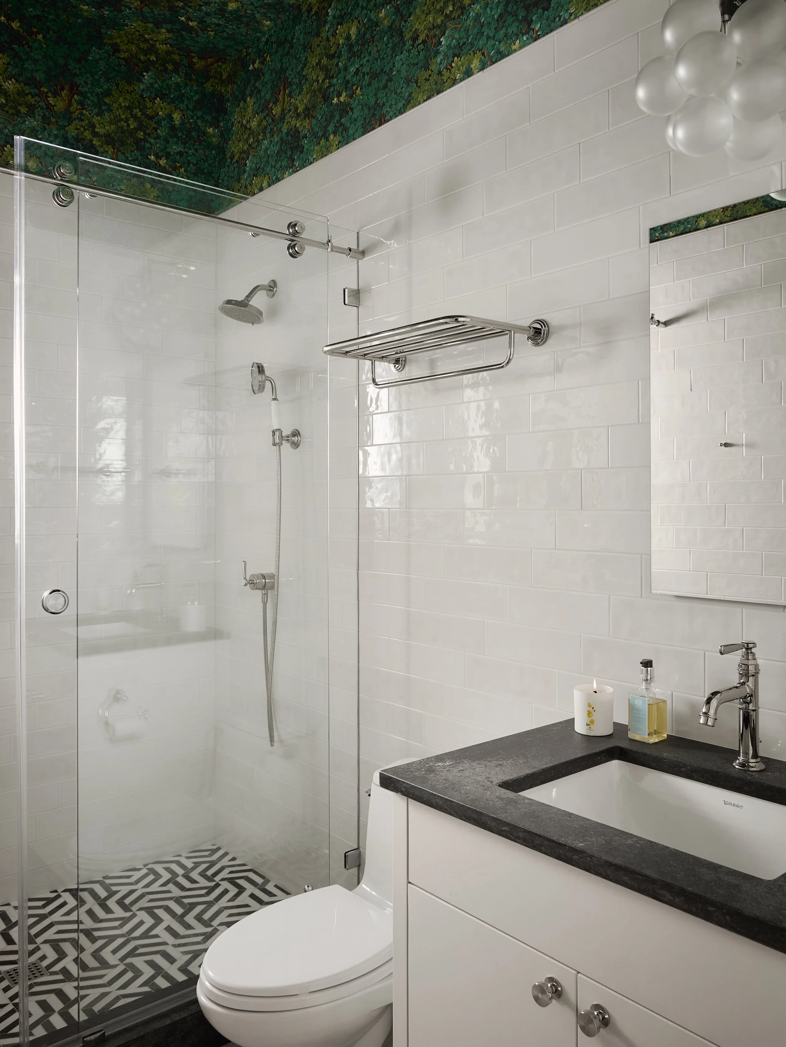 Bathroom with a glass-enclosed shower area, white subway tile walls, a black countertop with a white sink, a mirror, and a small candle and soap dispenser on the counter.