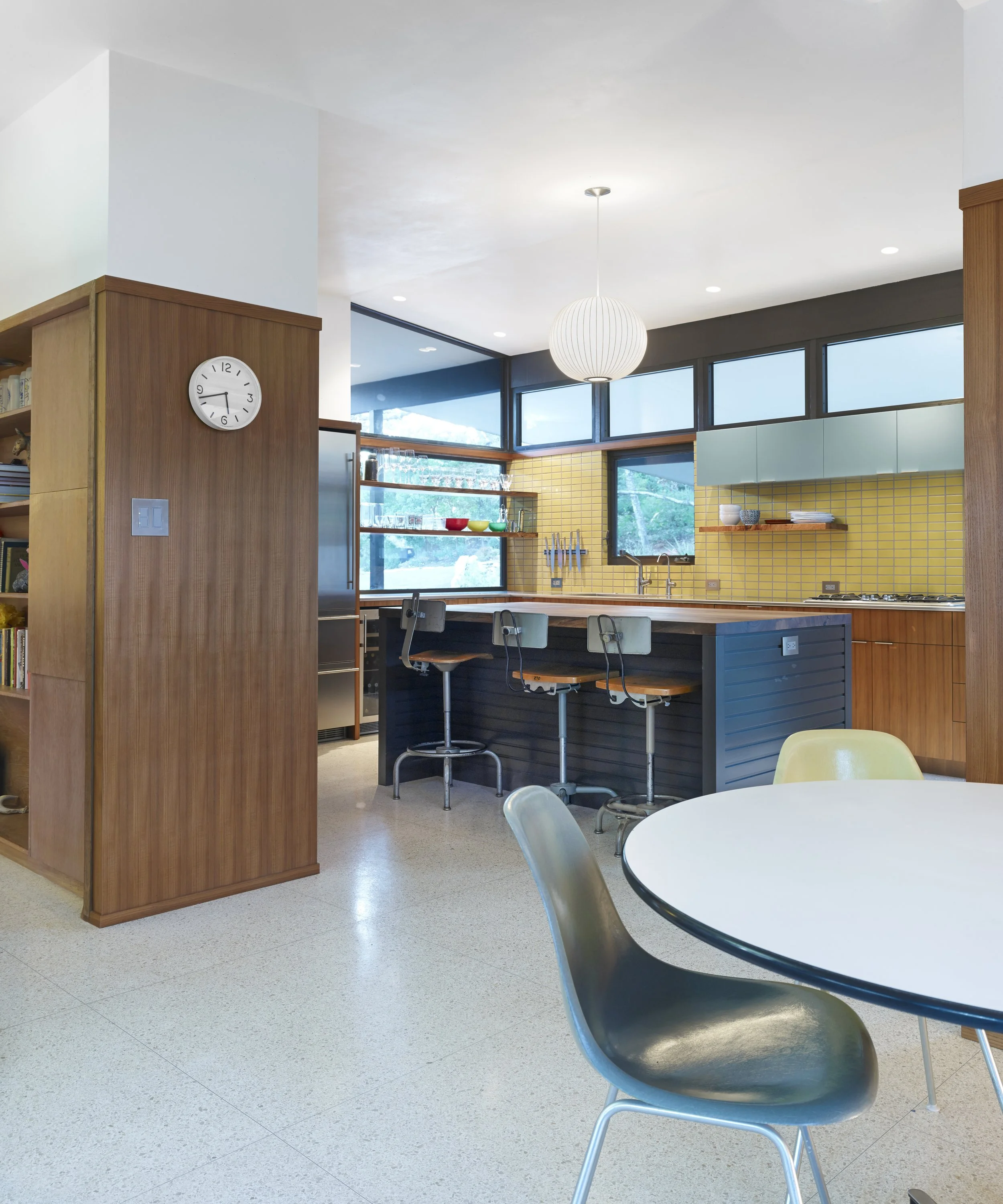 Austin architecture. Mid-century Modern kitchen with wooden accents, yellow tiled backsplash, and a round dining table with colored chairs.