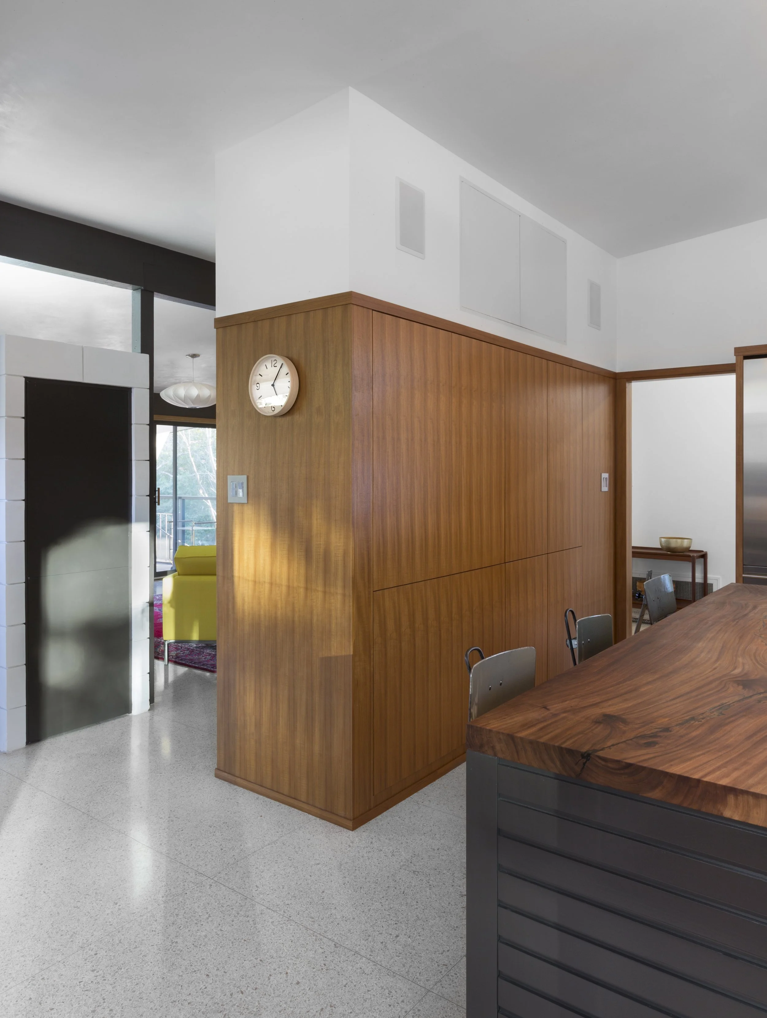 Austin architecture. Mid-century Modern Interior view of a modern home with a wooden wall, a wall clock, and a dining table with chairs, featuring a mix of wood and white walls and large windows.