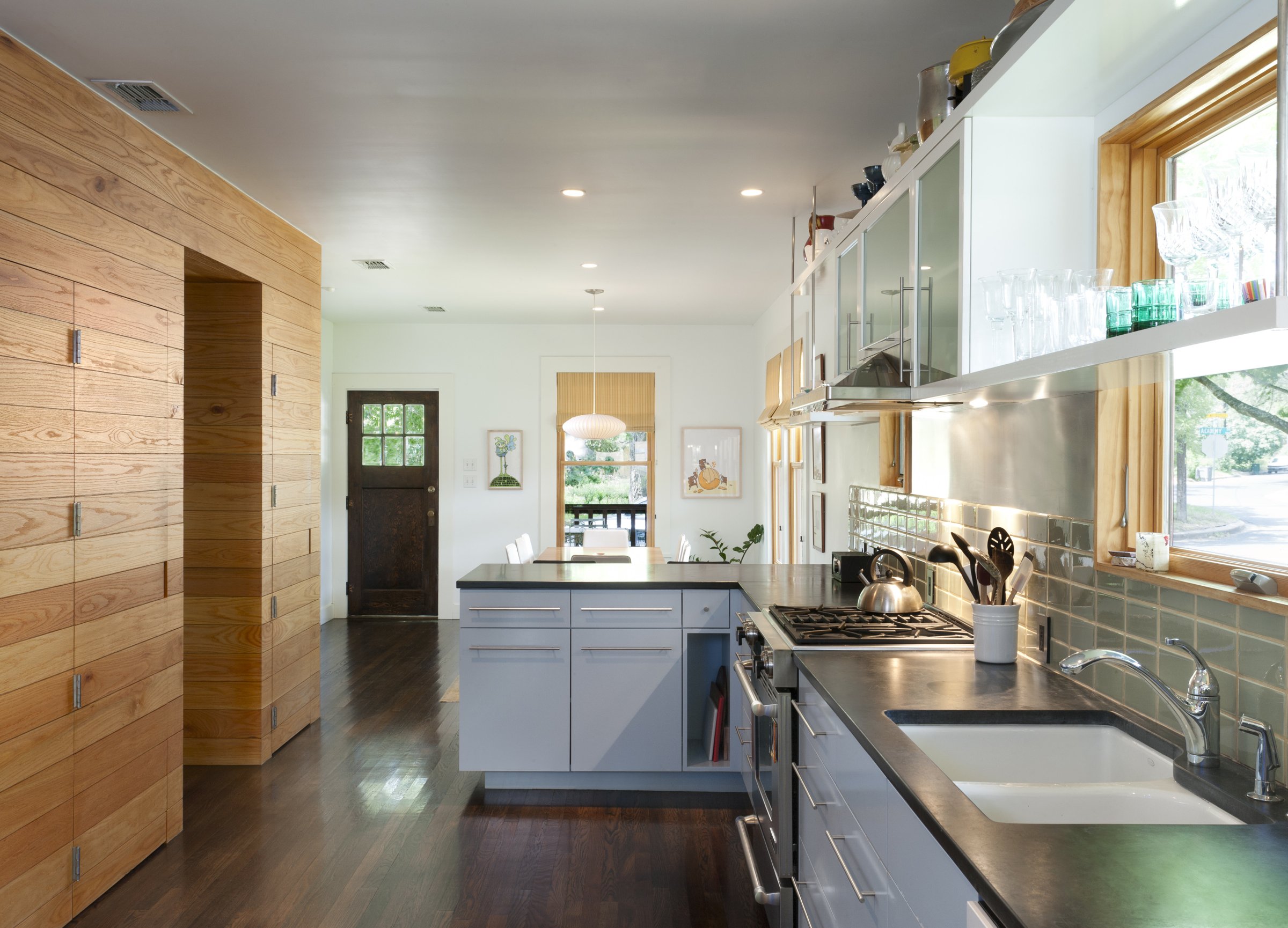 Austin architecture. Modern kitchen with wooden cabinets, stainless steel appliances, and a dark wood floor, opening to a dining area with natural light.