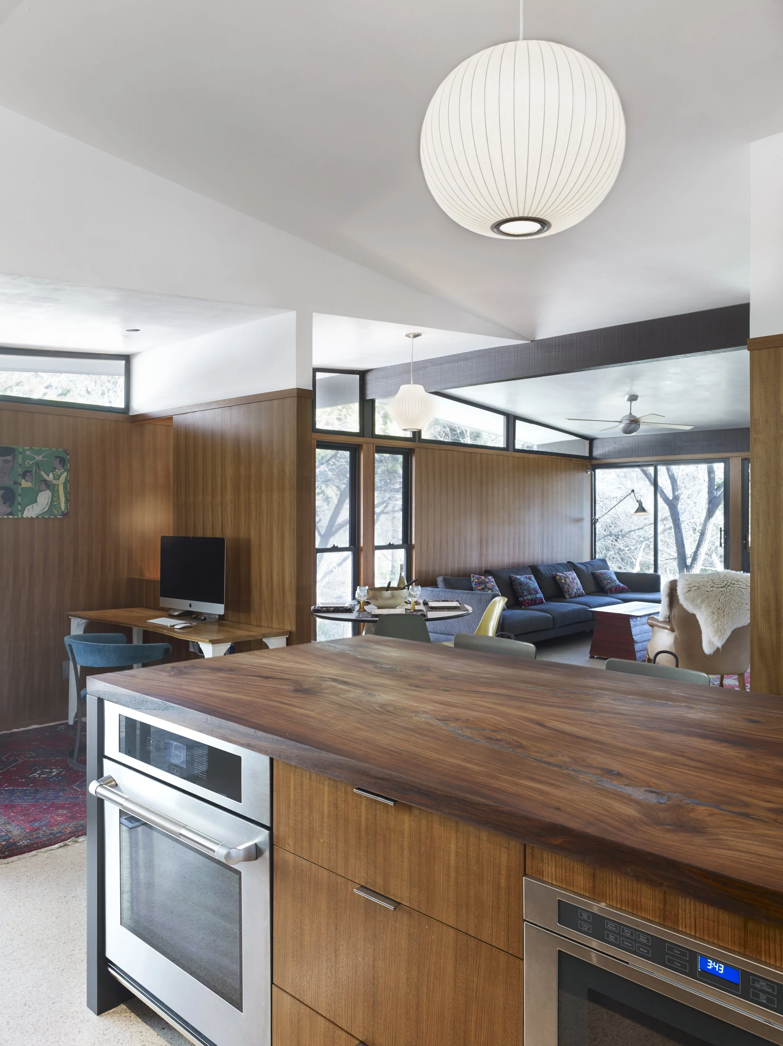 Austin architecture. Mid-century Modern Open-concept living space with wooden accents, large windows, modern kitchen appliances, and mid-century furniture.