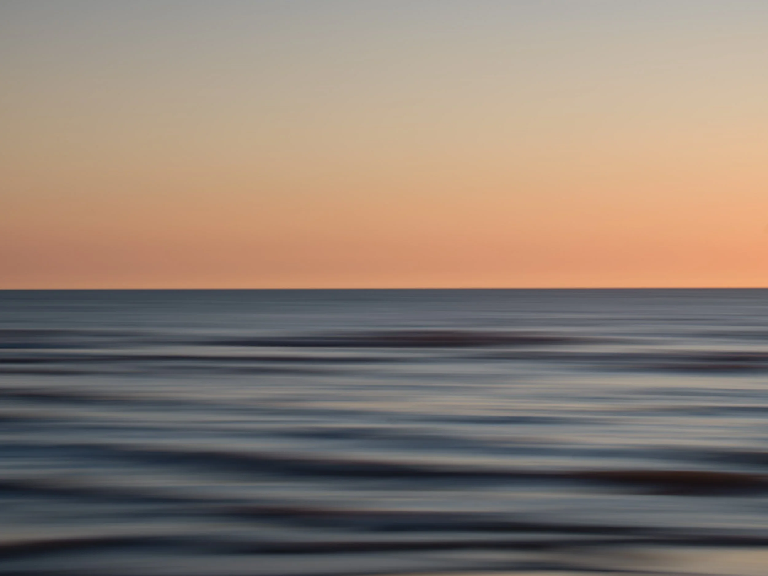 Abstract image with horizontal streaks in black, gray, and orange colors, resembling motion blur or a sunset over water.