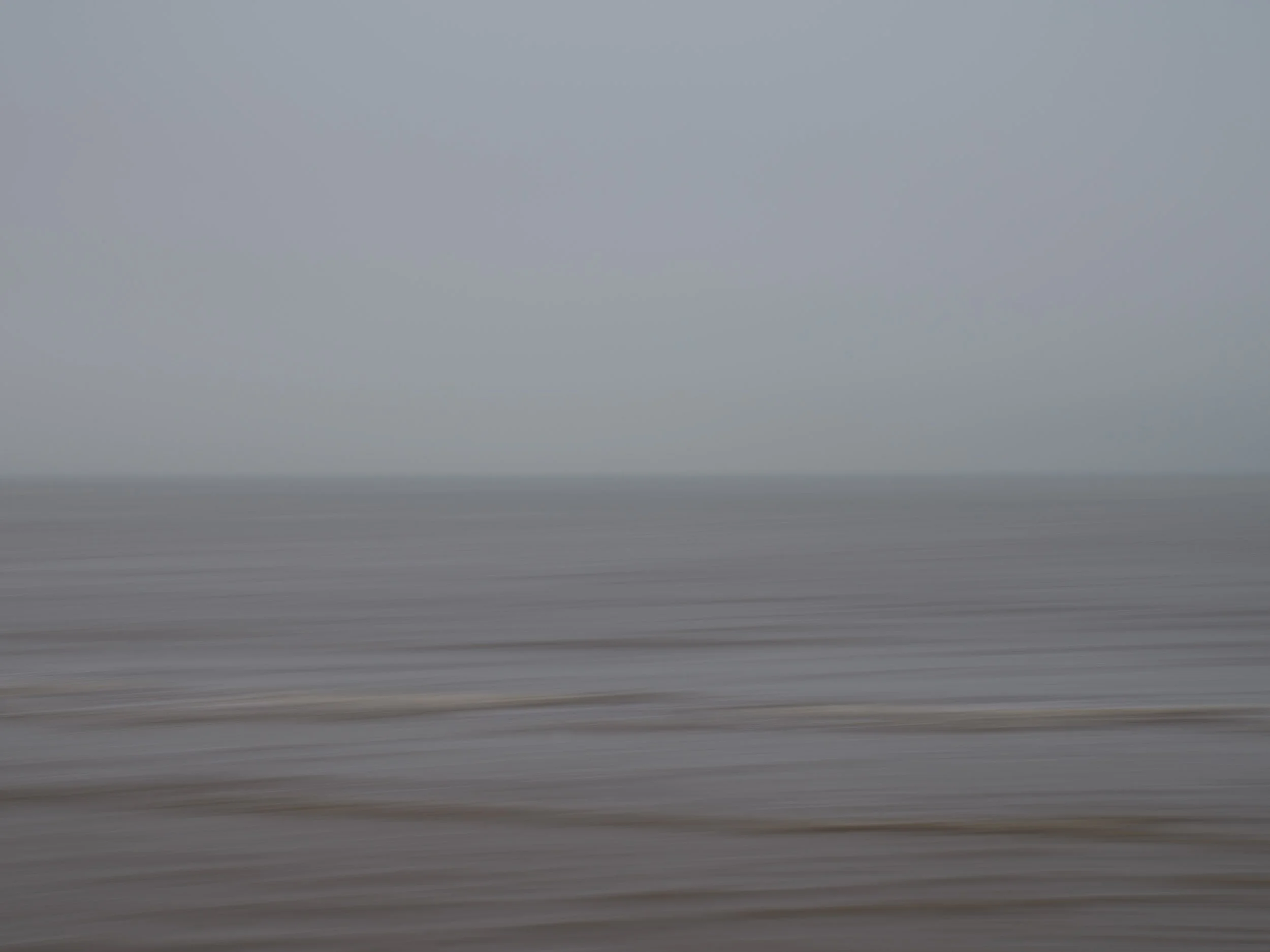 a blurred view of a landscape with a grey sky and a horizon line, possibly over the ocean or a large body of water