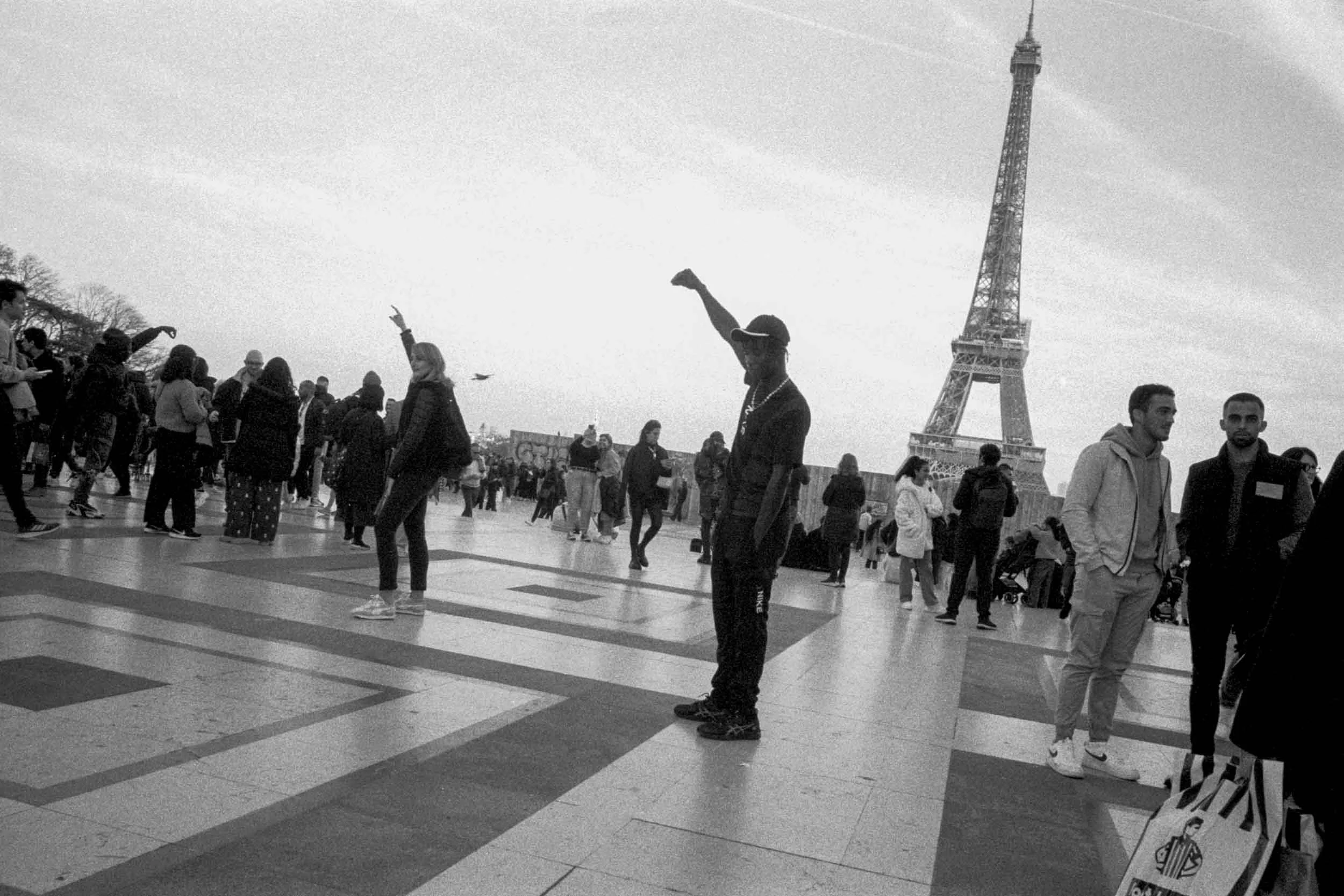 A crowded outdoor area with people walking and standing, near the Eiffel Tower in Paris, France.