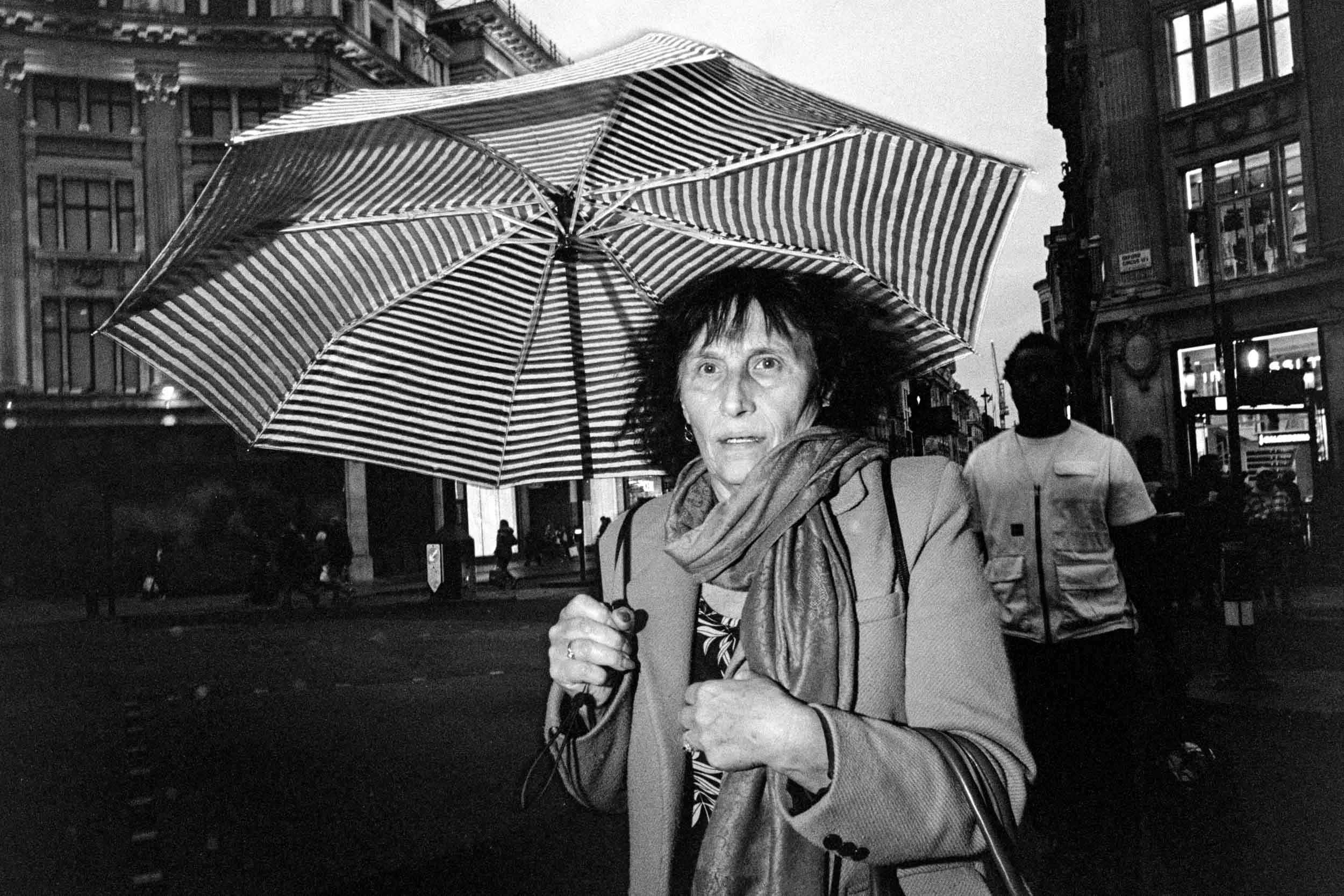 Street photograph using flash of a woman crossing the road at London's Oxford Circus. It is raining and she has an umbrella up.