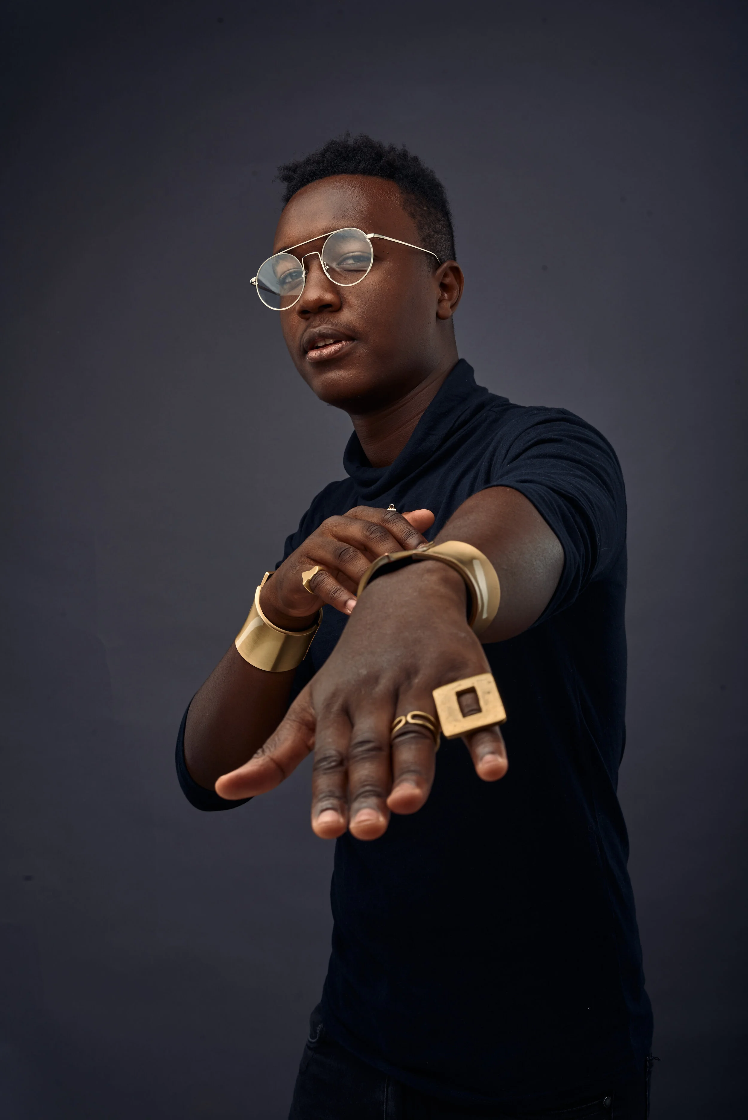 Person wearing glasses and gold jewelry posing with outstretched hand