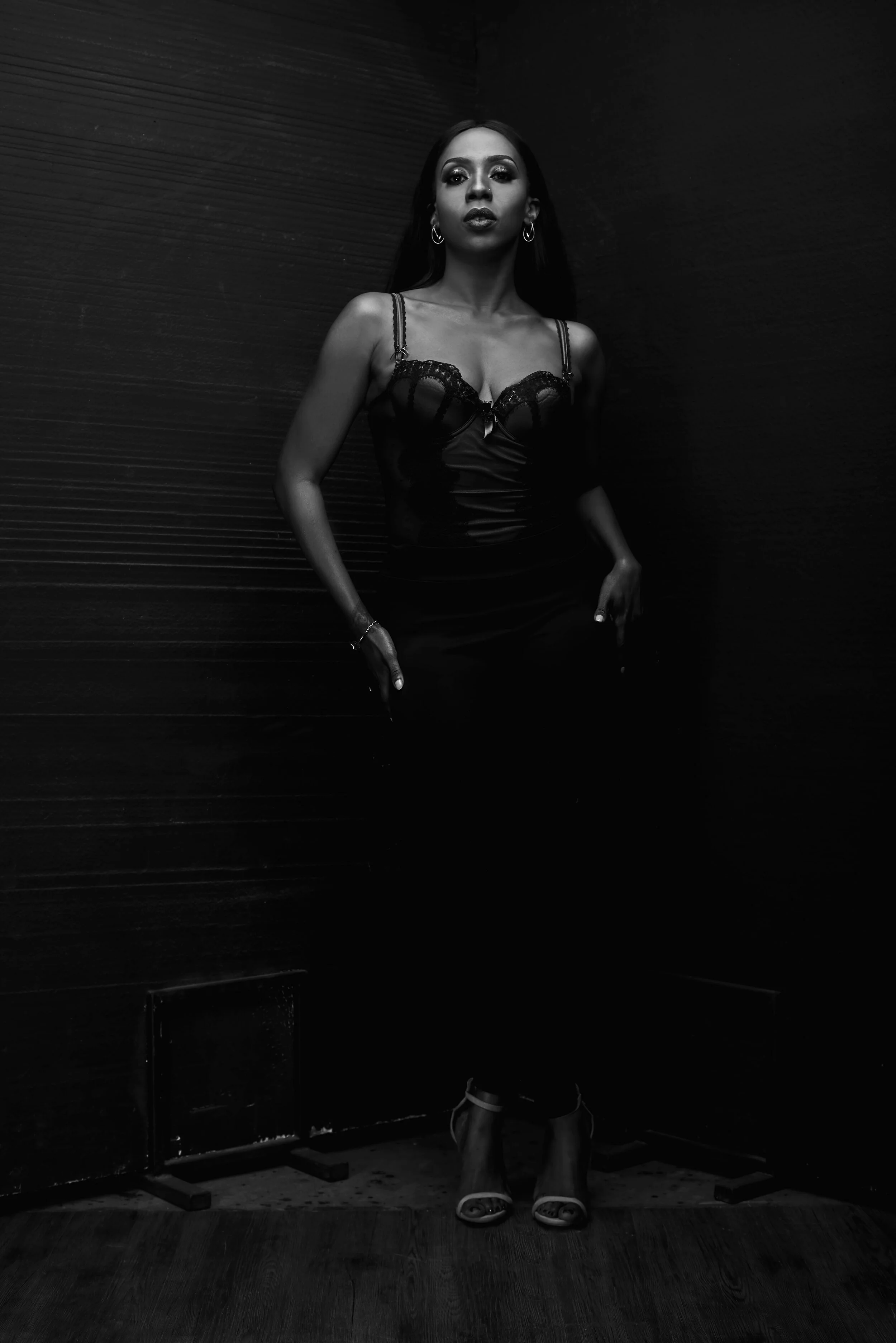 Black and white photo of a person in a fitted top and pants, standing against a textured dark background.