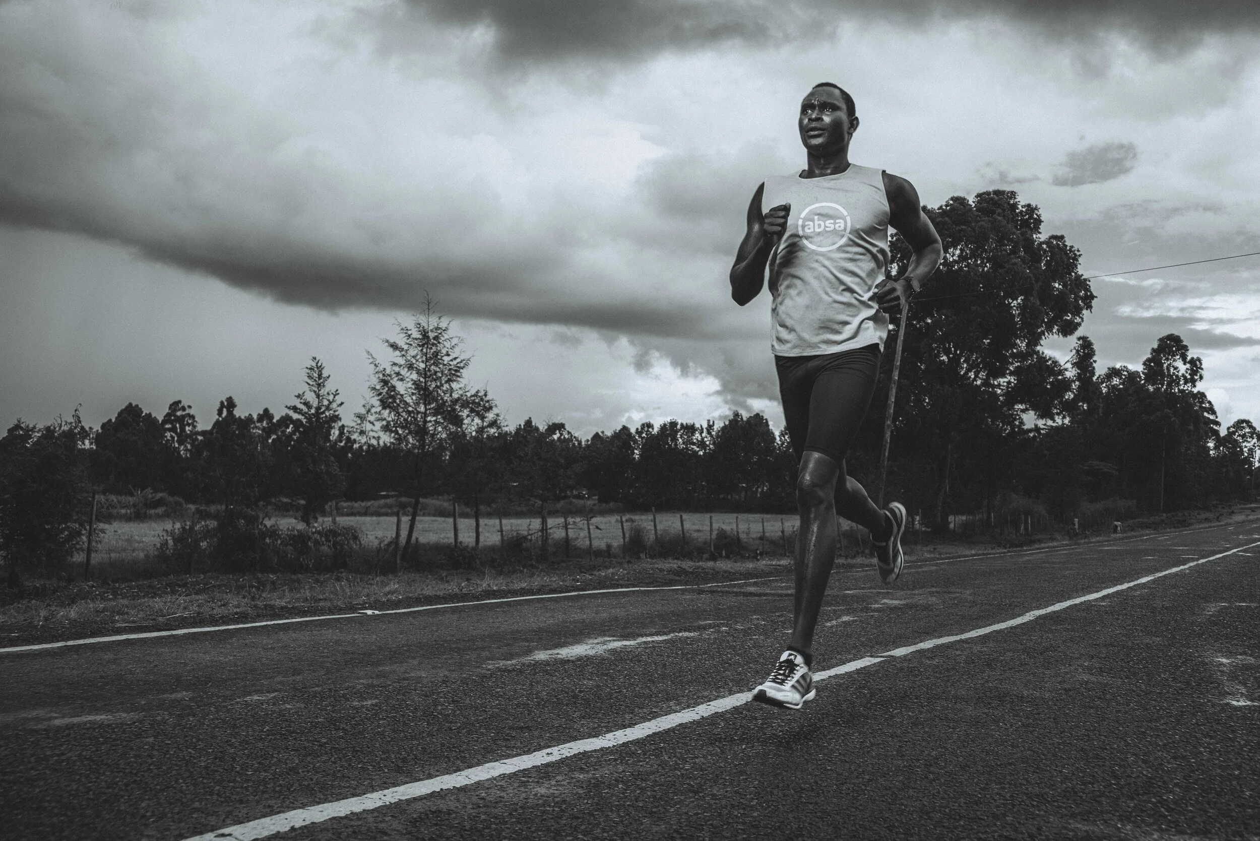 Black and white photo of a person running on a road with a cloudy sky backdrop.