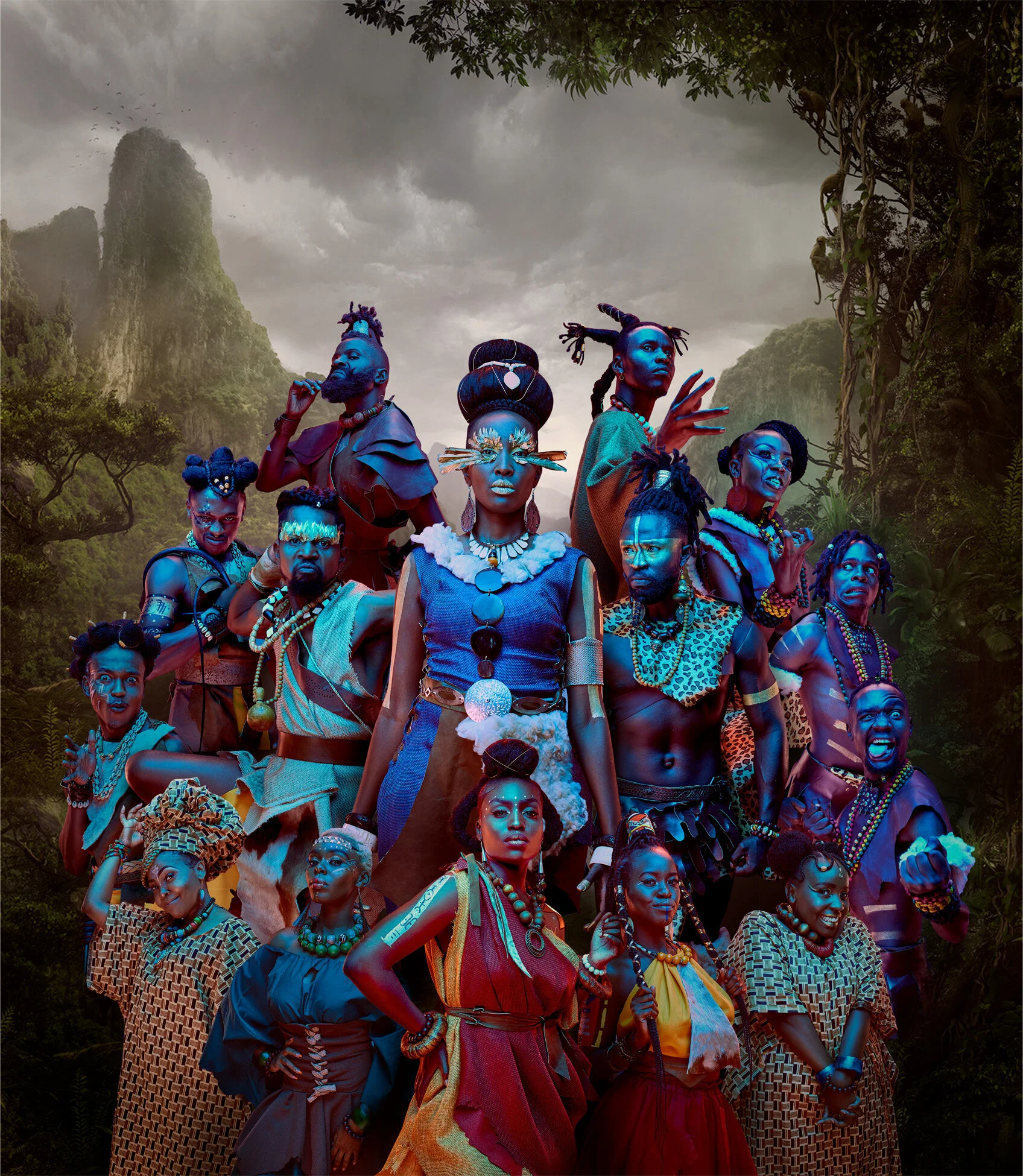 A group of people in colorful, tribal-inspired attire stand in front of a misty, mountainous jungle backdrop. They are adorned with accessories and body paint, showcasing a variety of hairstyles.