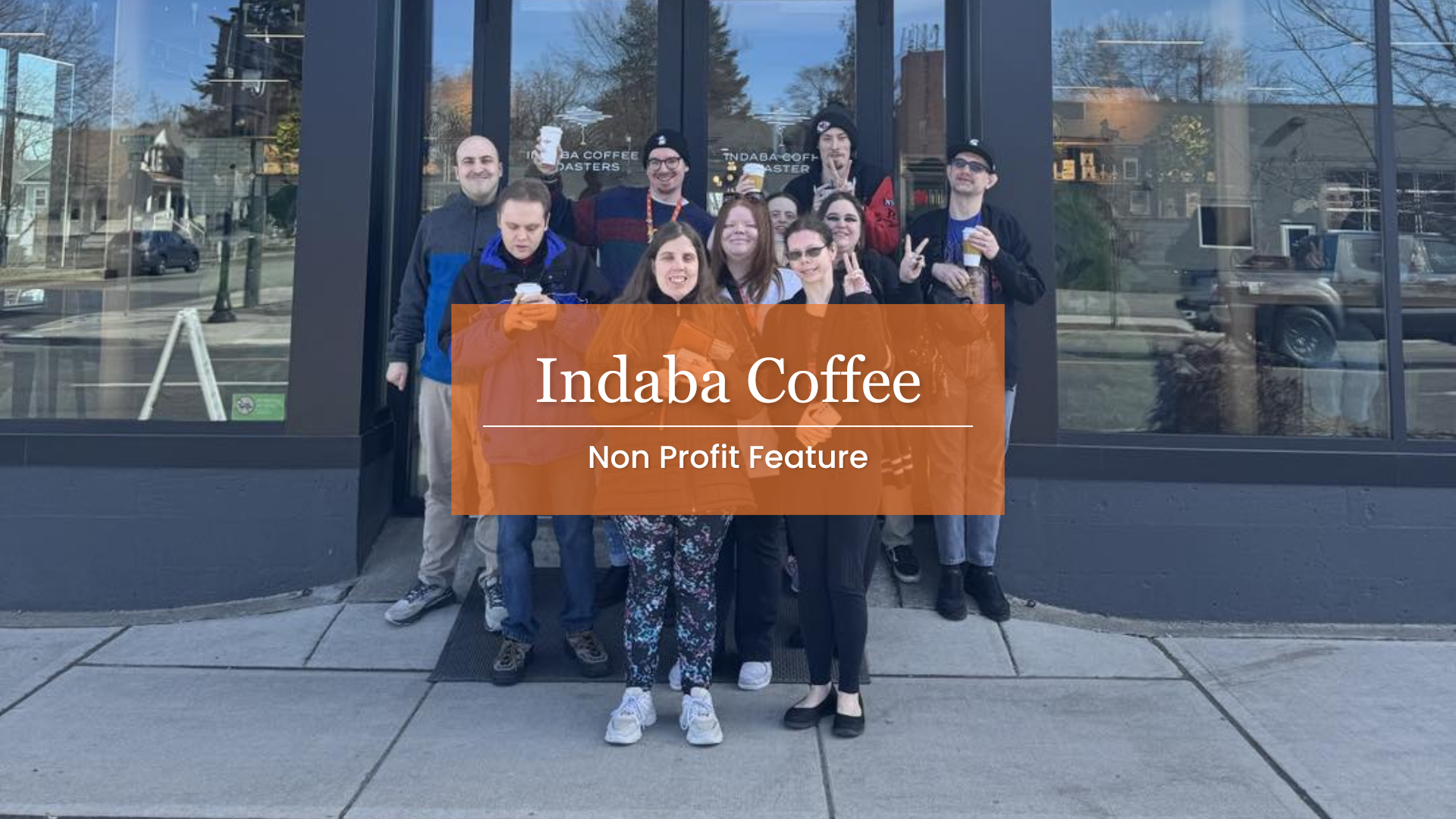 Indaba Coffee Non Profit Feature. Image Description: Members of The Arc's community center stand in front of Indaba coffee smiling and waving at the camera as they hold their drinks