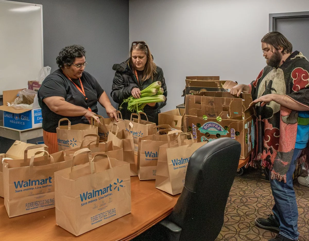 The Arc of Spokane staff sort fresh celery and produce from 2nd Harvest Zilch into brown bags on a large table. Three team members work together in a focused, indoor office setting. A meaningful, hands-on community impact and culture moment.