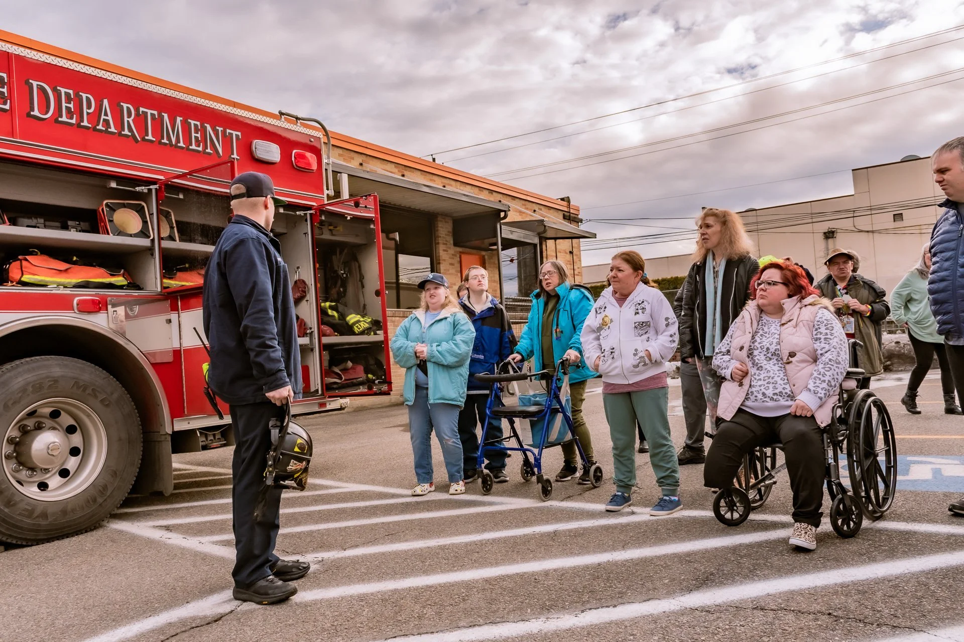 A Spokane Fire Department Station 1 Firefighter stands in front of six Community Center members outside of The Arc of Spokane on an overcast day