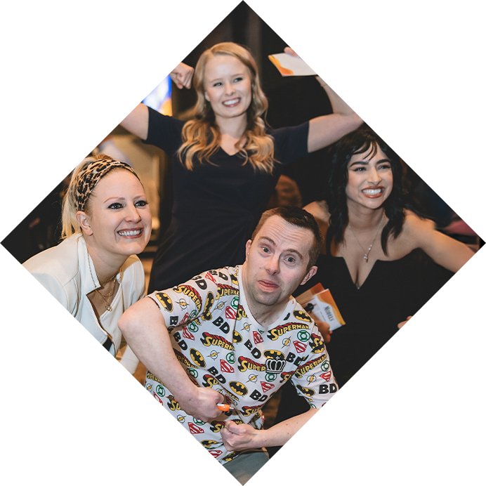 A group photo of a masc presenting Rock the Runway model surrounded by three femme presenting guests. They are all smiling and doing silly poses.