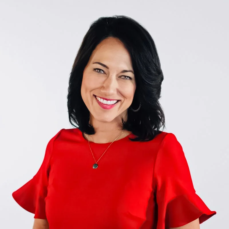 Kalae Chock, Spokane news anchor for KHQ, smiles in a red blazer and silver jewelry against a blurred studio background.