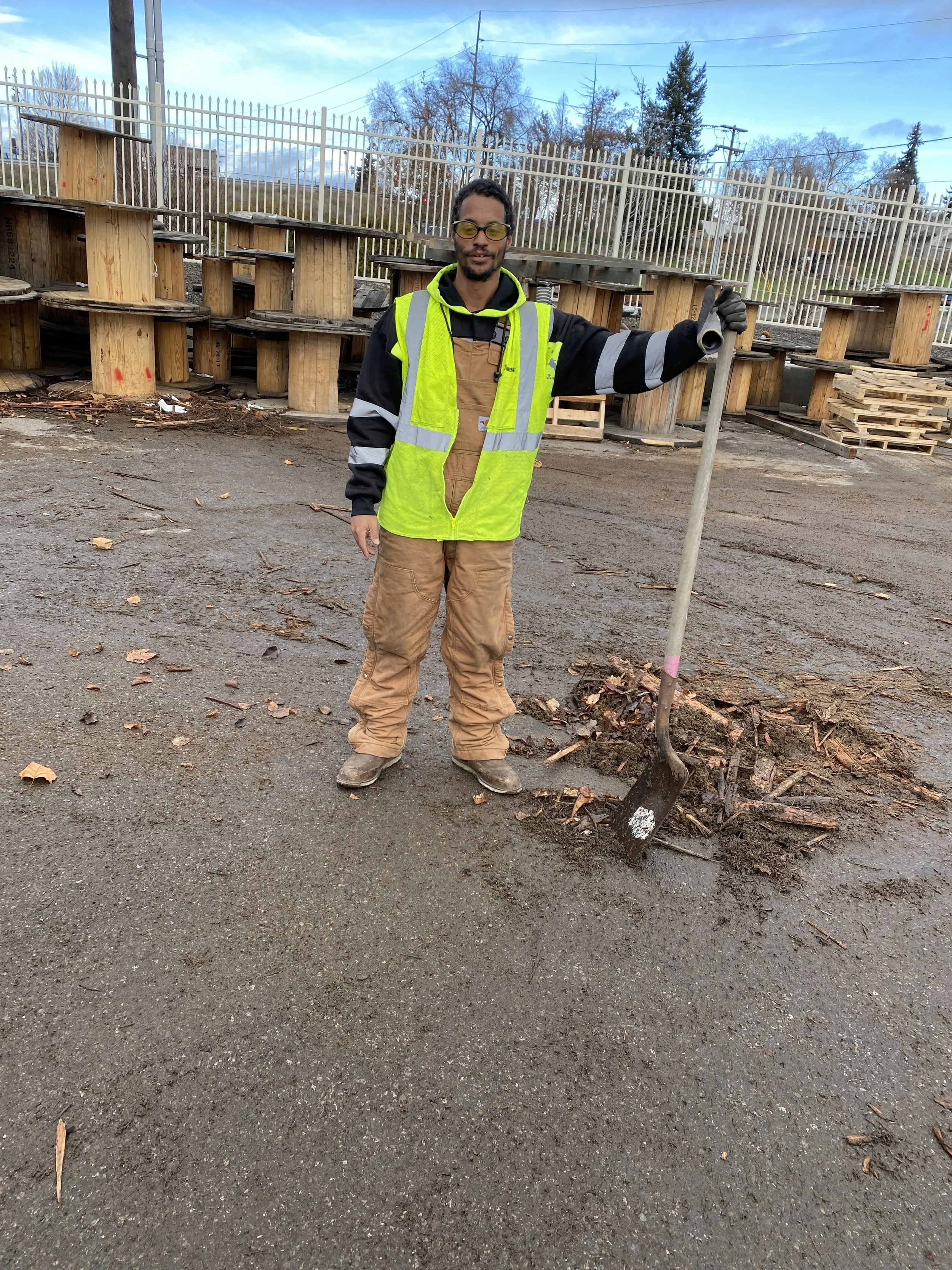 Image of James McCormack. He holds a shovel while working outside Avista's Investment Recovery Center. He wears a reflective yellow vest over Carheart overalls and a warm jacket with reflective sleeves.
