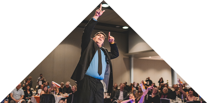 A 2025 image of a masc presenting Rock the Runway model. He is wearing a suit and tie and poses for the audience.