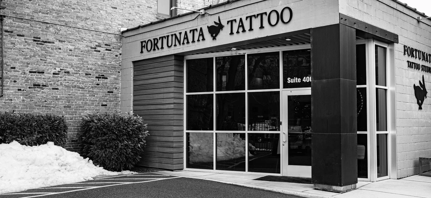 Exterior of Fortunata Tattoo in Spokane, showing the front entrance, large windows, and building signage in black‑and‑white.