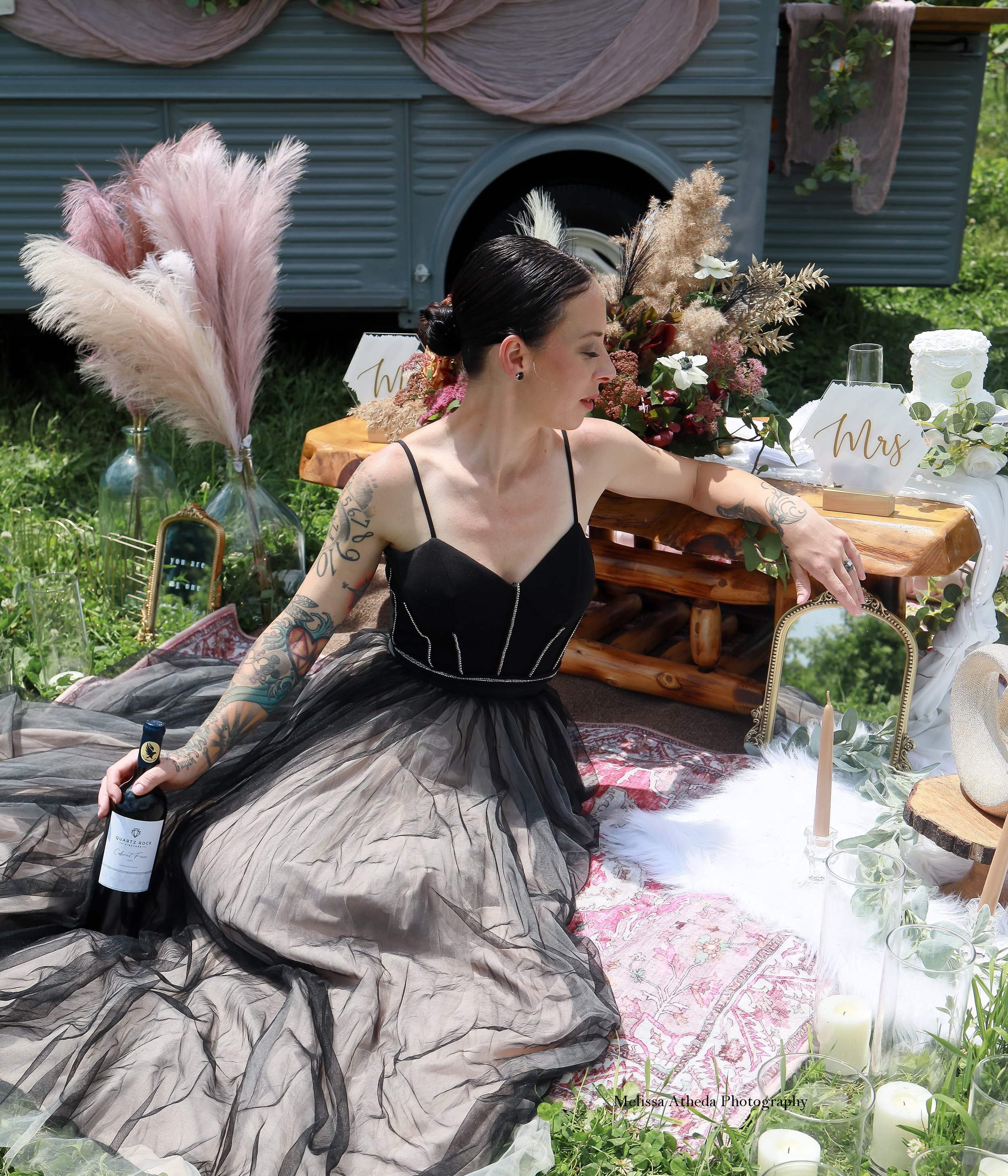 Woman in a black dress holding a bottle of Quartz Rock Vineyard wine and sitting with flowers