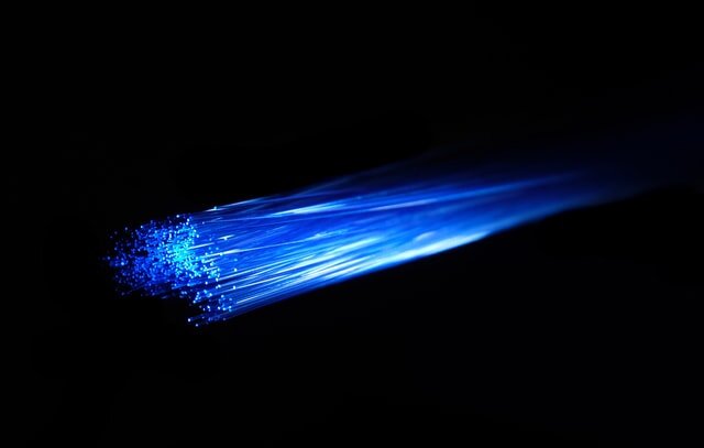 Blue light illuminates the thin glass threads of a fibre optic cable. Each cable is able to transport light/information across long distances via internal reflection (similar to the way a mirror can direct light). To find out more check out:  Fiber optic cables: How they work.  Photo by Compare Fibre on  Unsplash .