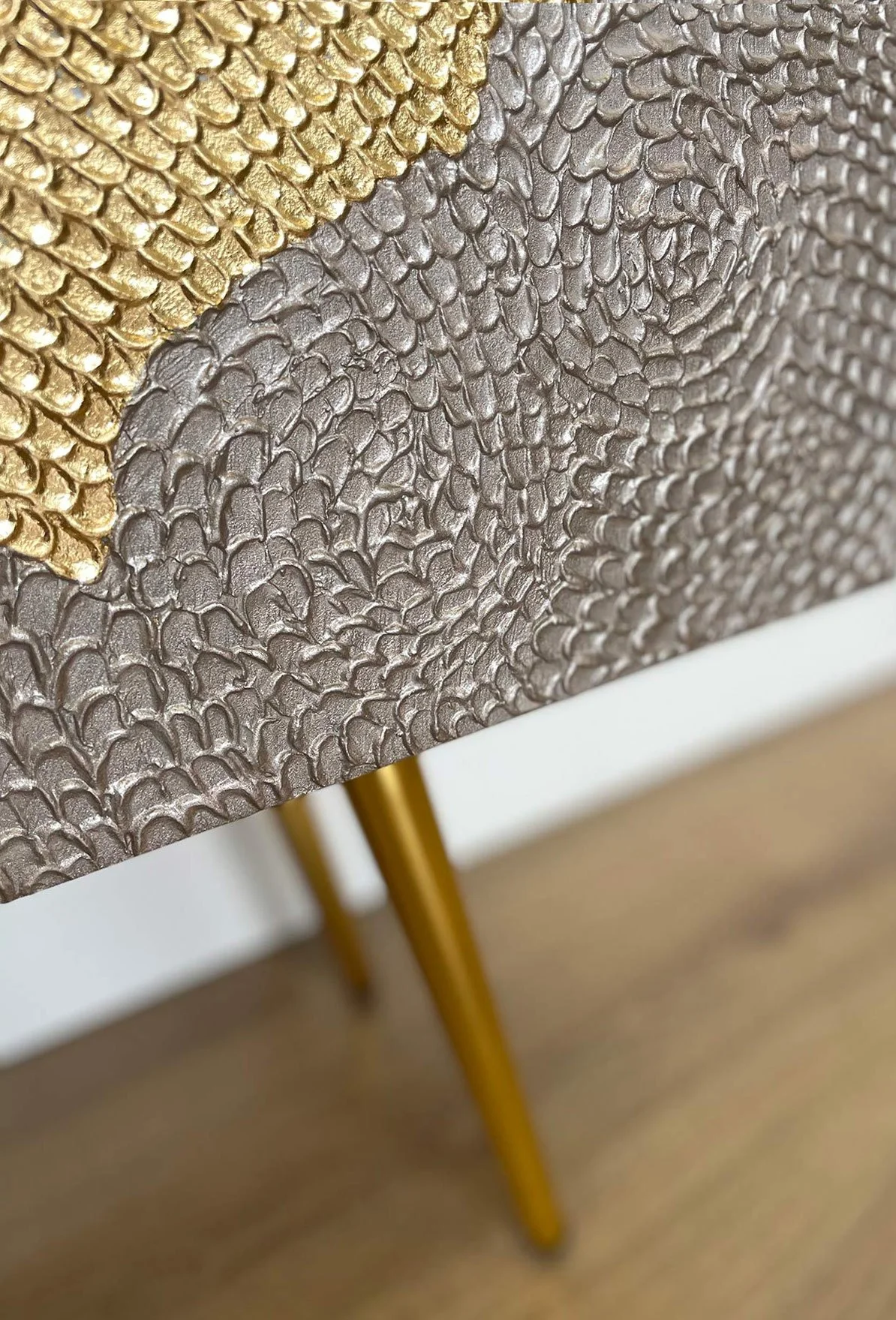 Close-up detail of the hand-sculpted botanical relief and antiqued gold leaf finish on a luxury sideboard door. Supported by a gold metal leg.