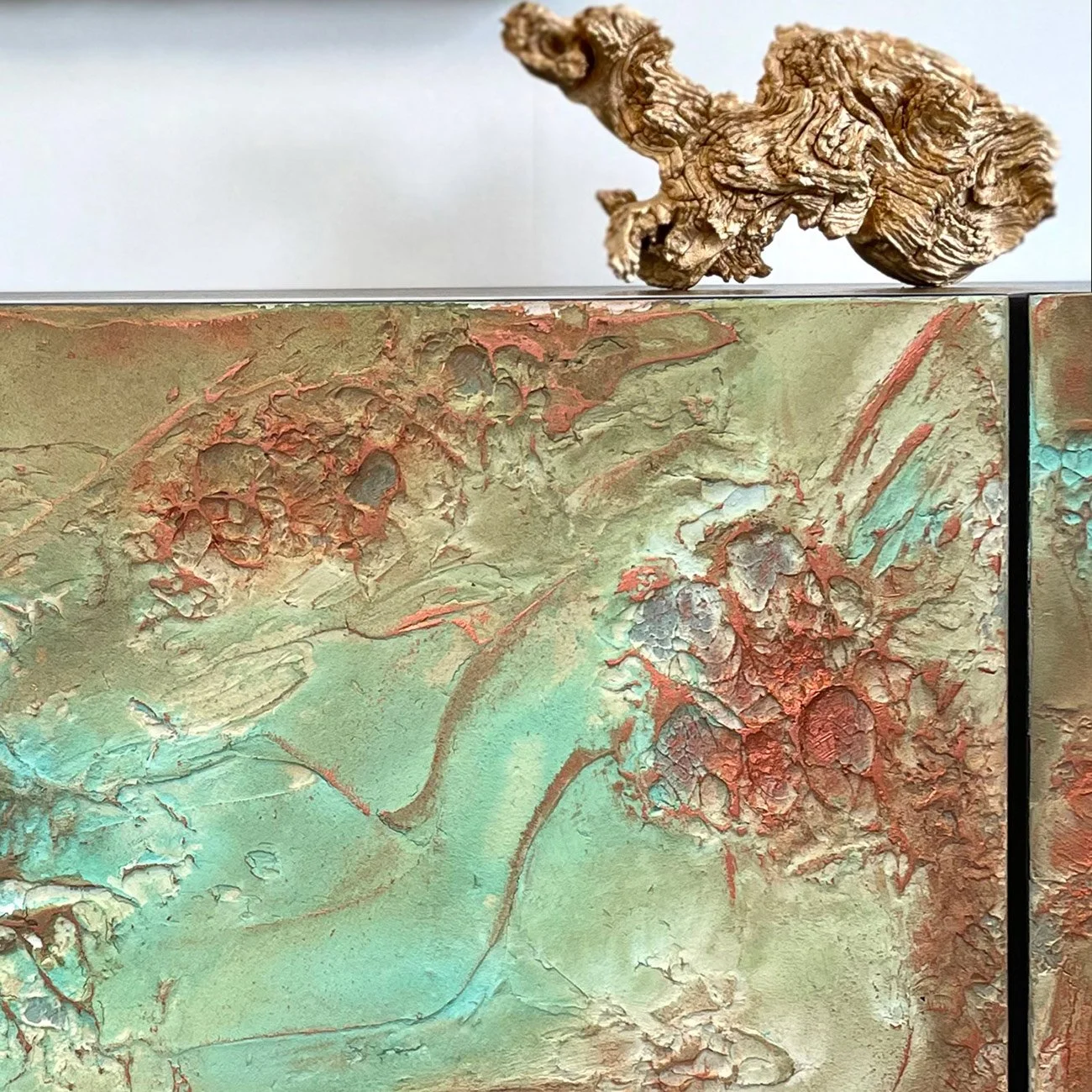 A macro detail shot focusing on the hand-sculpted relief, showing the deep ridges and the way the light catches the metallic azure and copper highlights within the green patina.