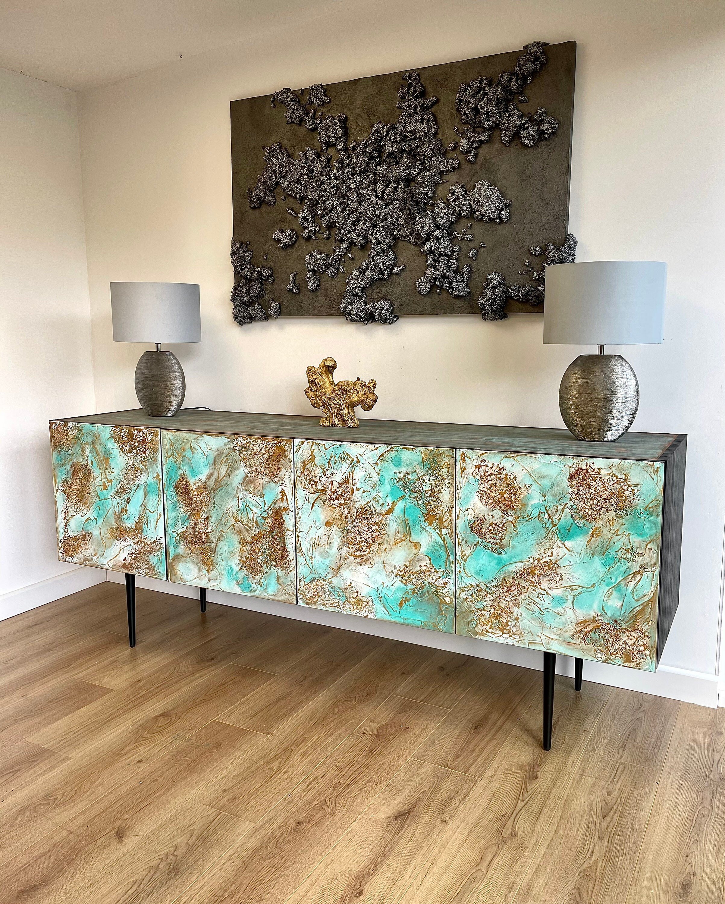 A modern, custom-made sideboard with a turquoise and gold abstract design stands in a room with wooden floors.