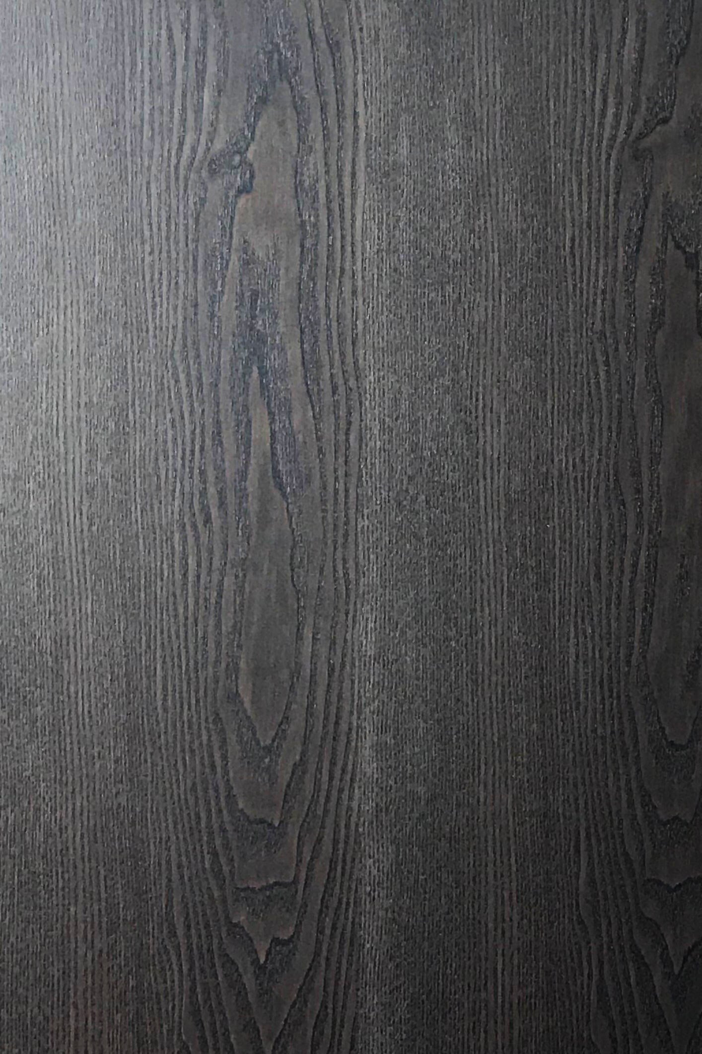 Close-up of a dark wood grain surface with prominent vertical lines and patterns, resembling textured art. The texture is slightly rough, displaying natural variations in tone and grain density.