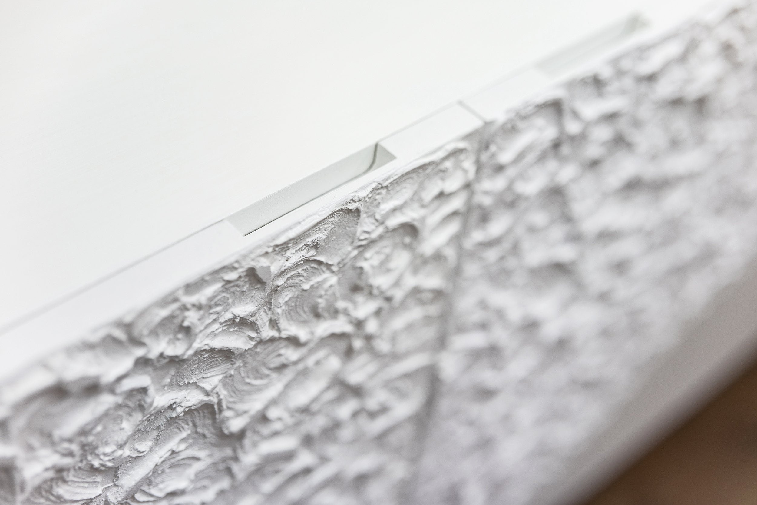 Close-up of a textured white surface with a rough, swirling pattern, likely part of bespoke furniture or cabinet. A small indentation or handle accents the top edge.