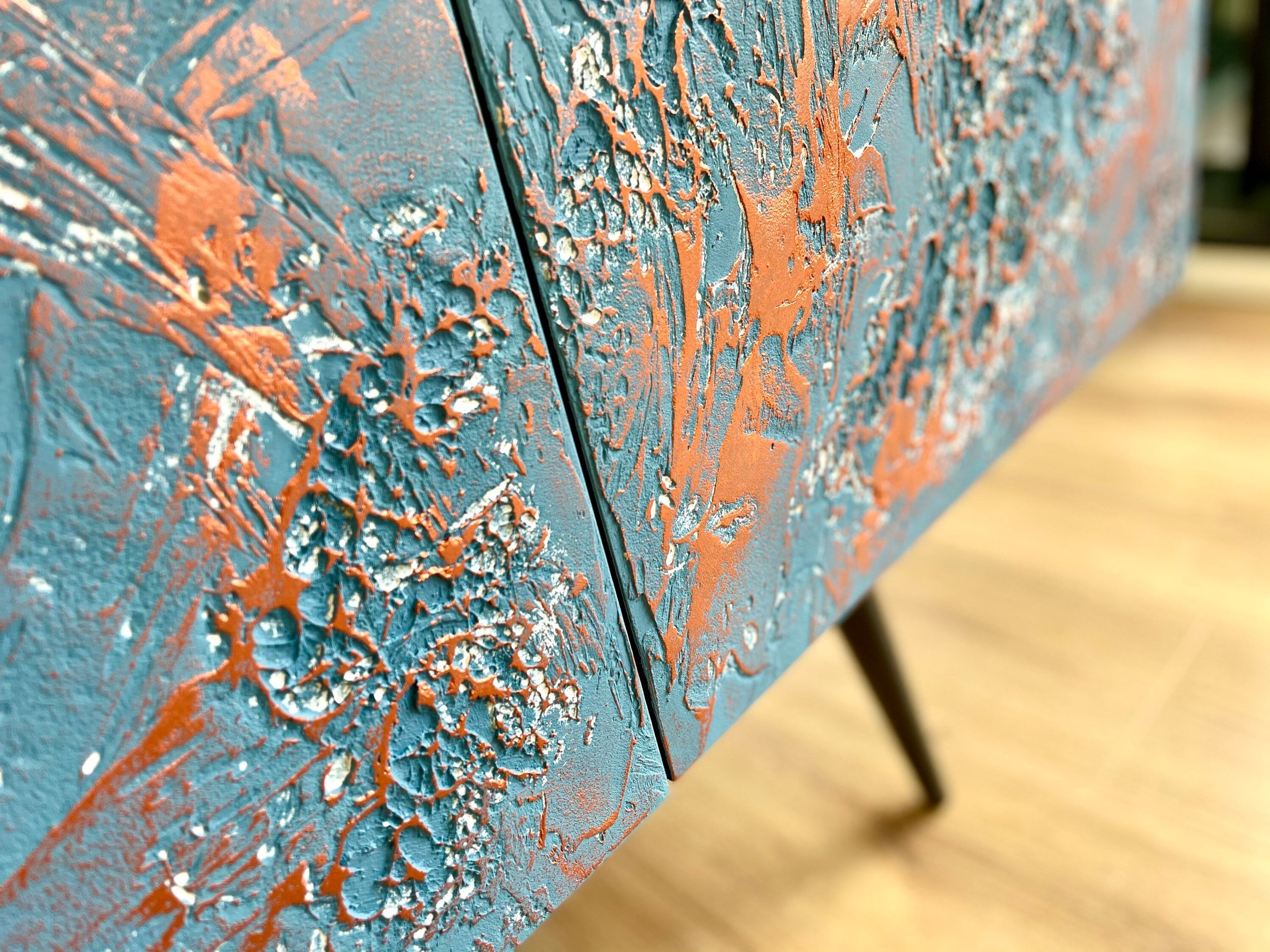 Close-up of a textured cabinet surface with a blue and orange abstract design. The raised, tactile patterns create the look of textured art, with contrasting colors adding depth.