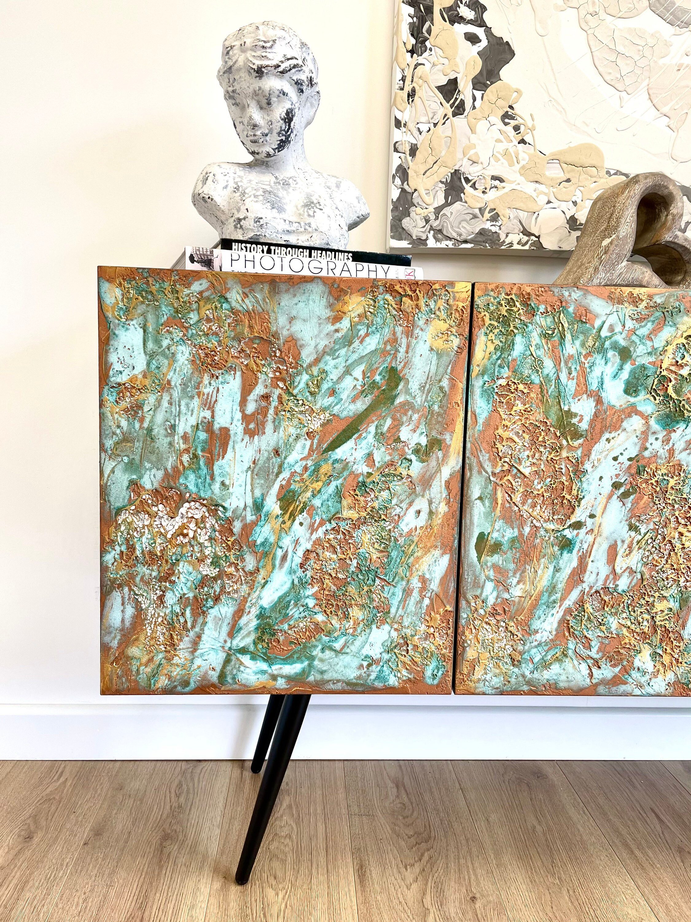 A custom-made sideboard with abstract green and gold textured doors stands on black angled legs.