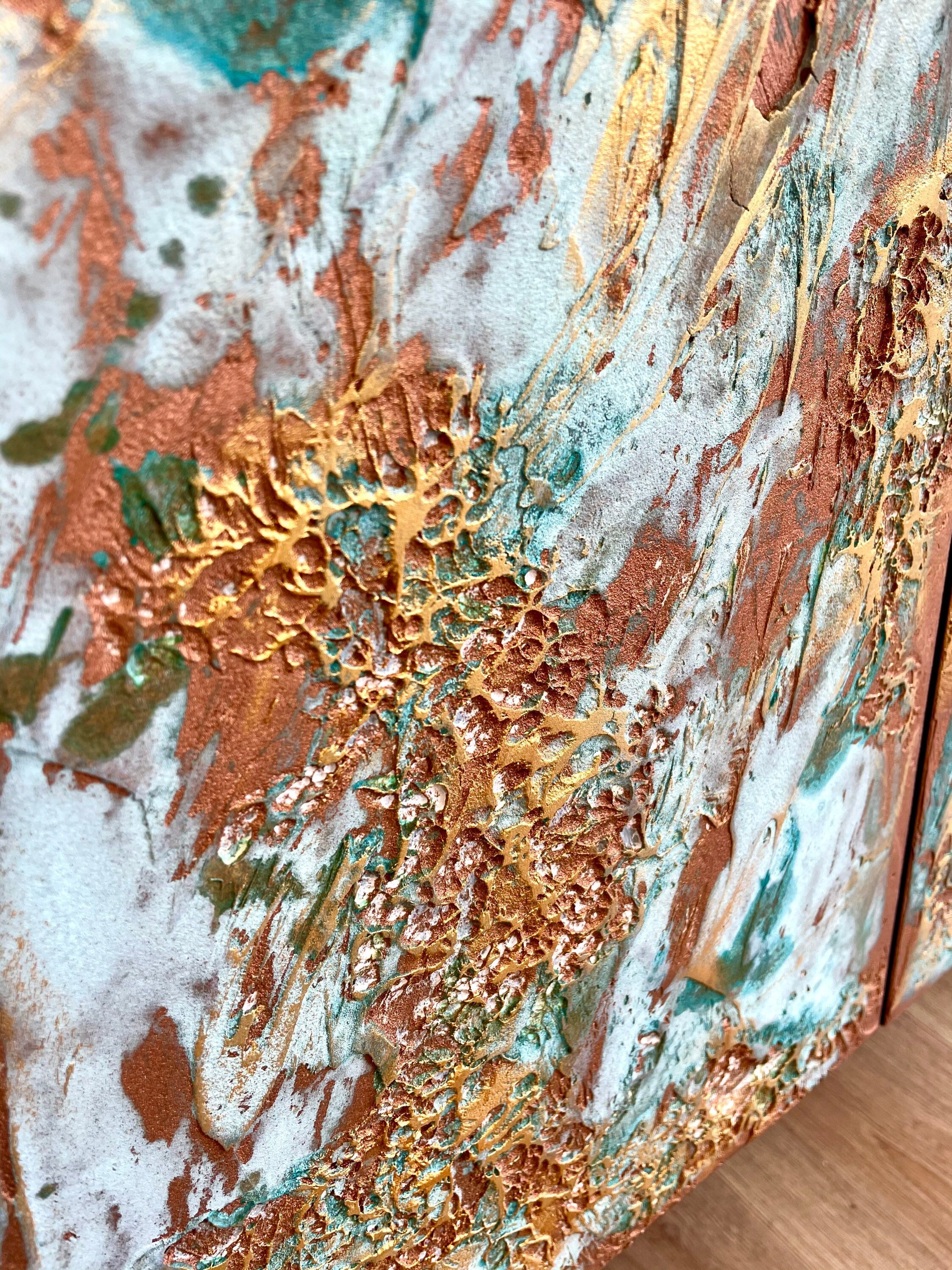 Close-up of an abstract painting with textured layers in metallic copper, teal, and white. The surface appears rough and tactile, much like bespoke furniture.