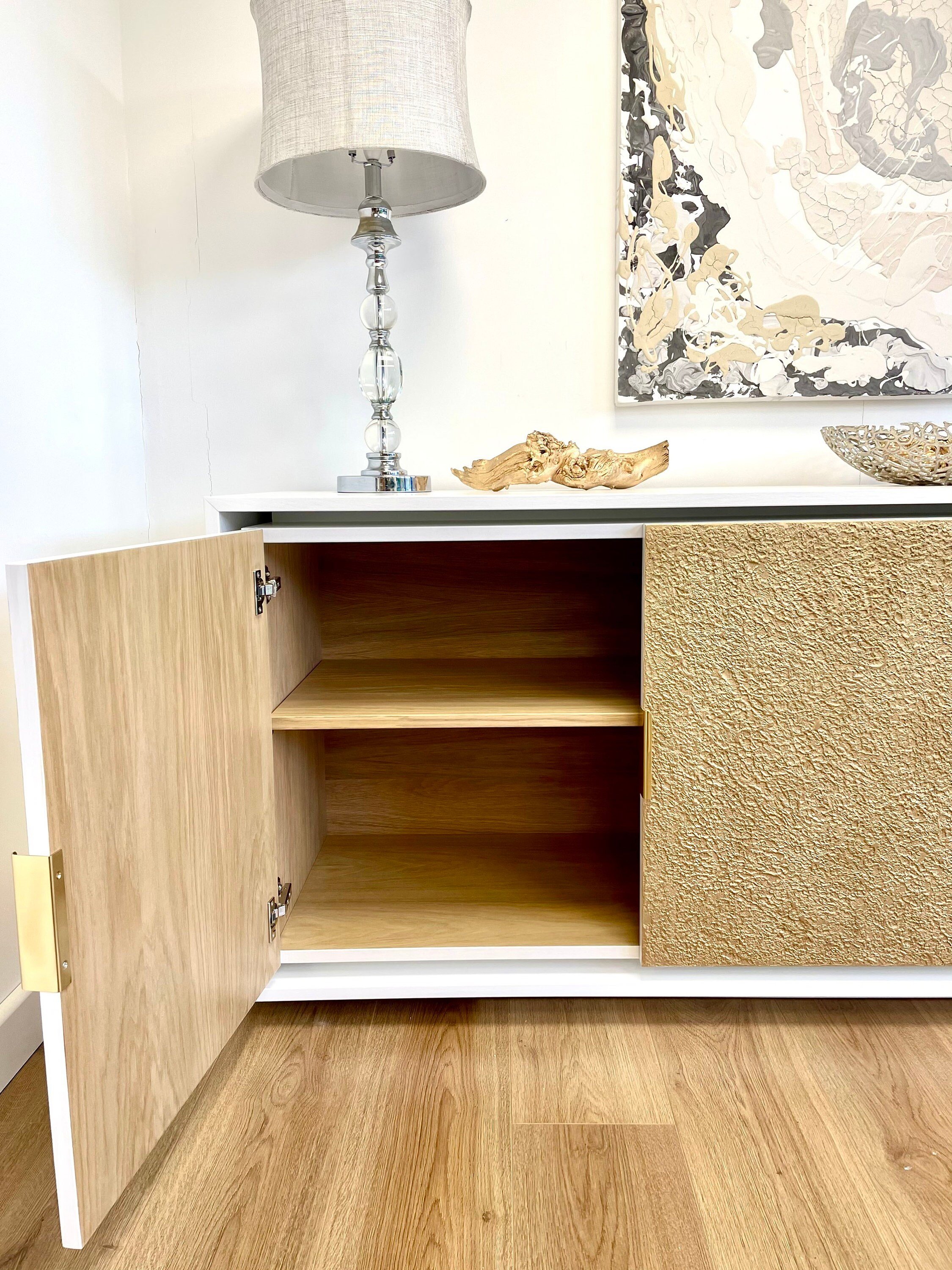 A custom-made sideboard with one door open reveals two interior shelves. The exterior showcases a blend of wood and textured surfaces.
