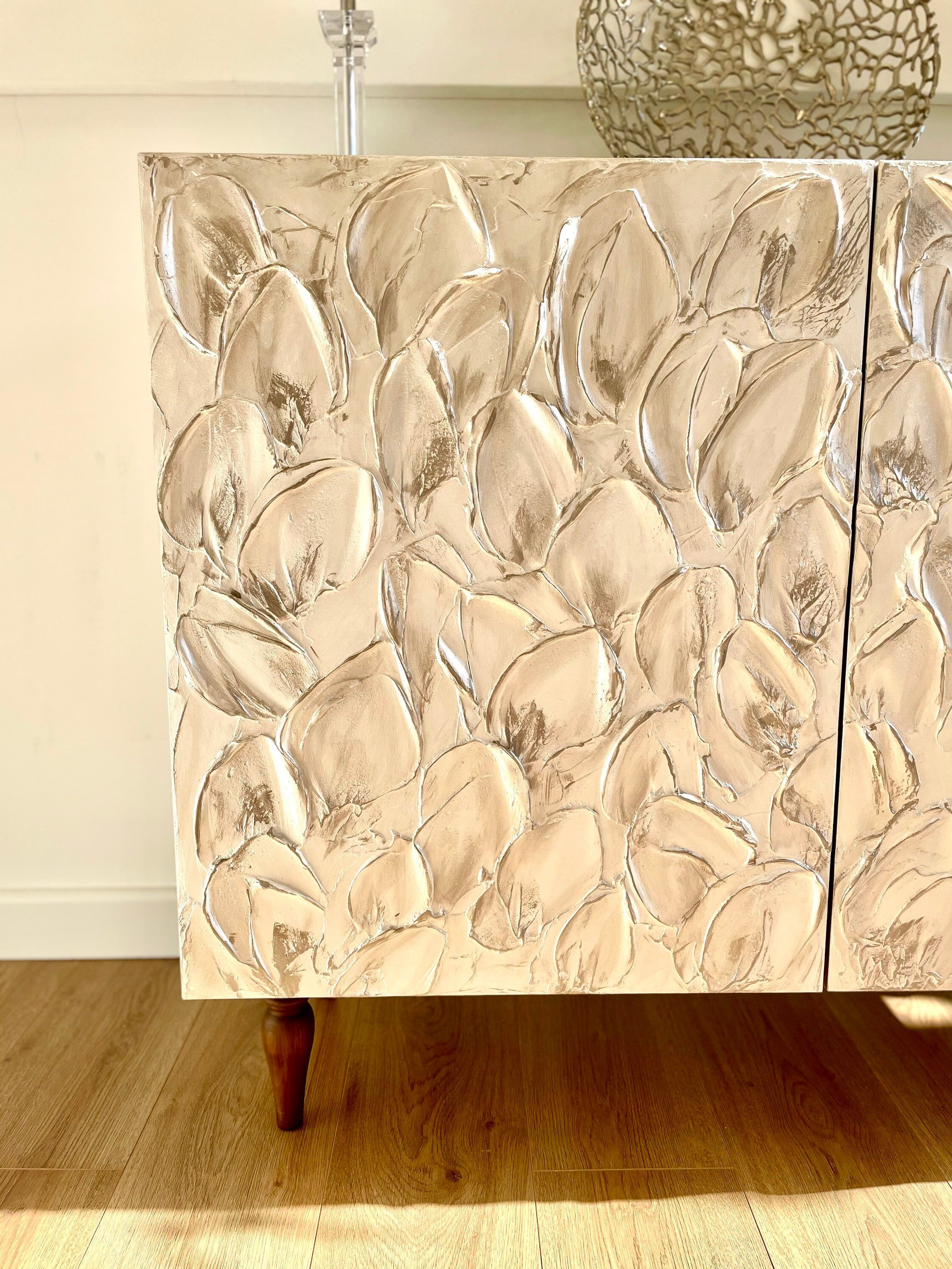 Textured art meets function in this custom-made sideboard with a raised leaf pattern in a metallic finish, set on wooden legs.