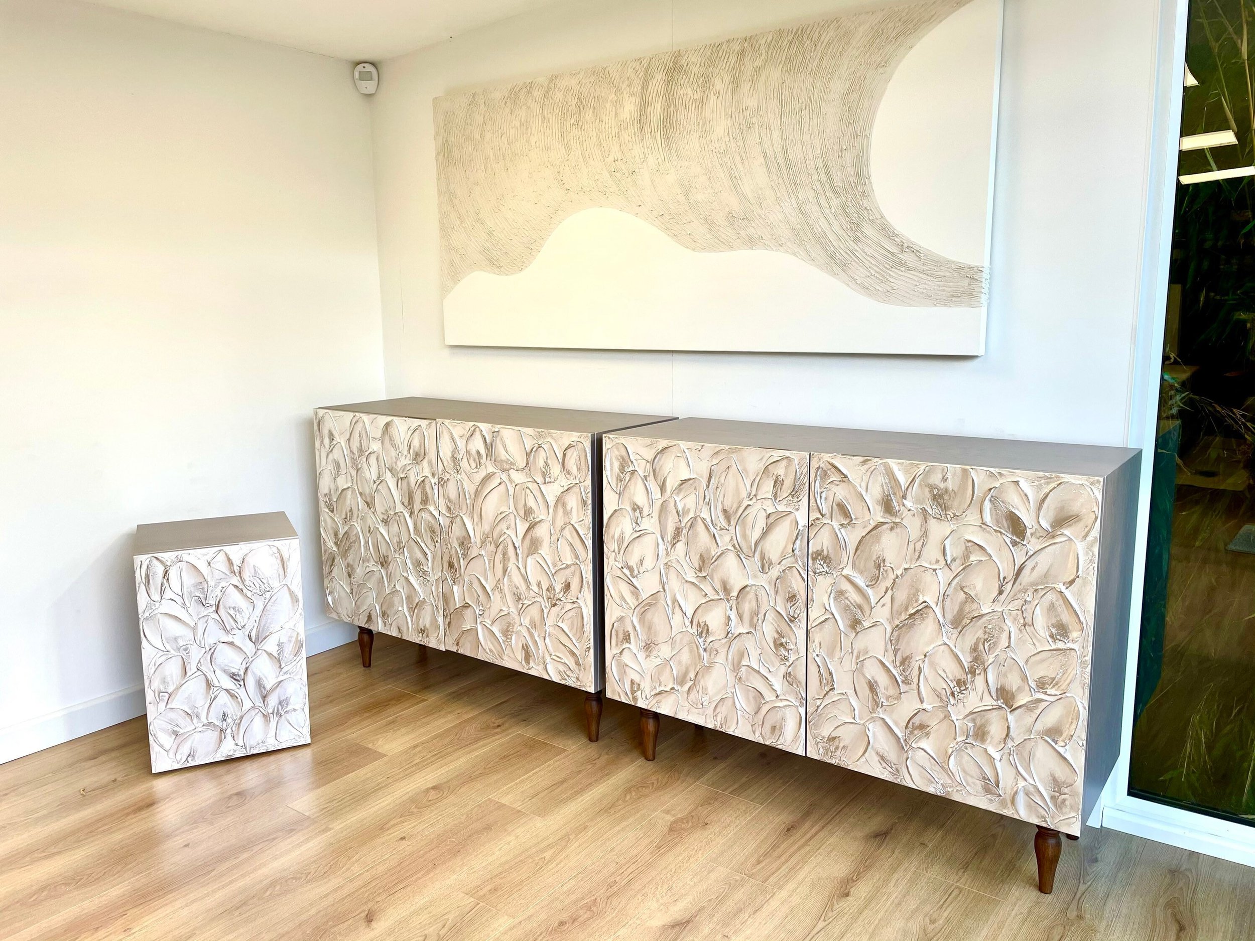 A modern room with light wooden flooring features a custom-made sideboard and a matching small cabinet in white and beige.