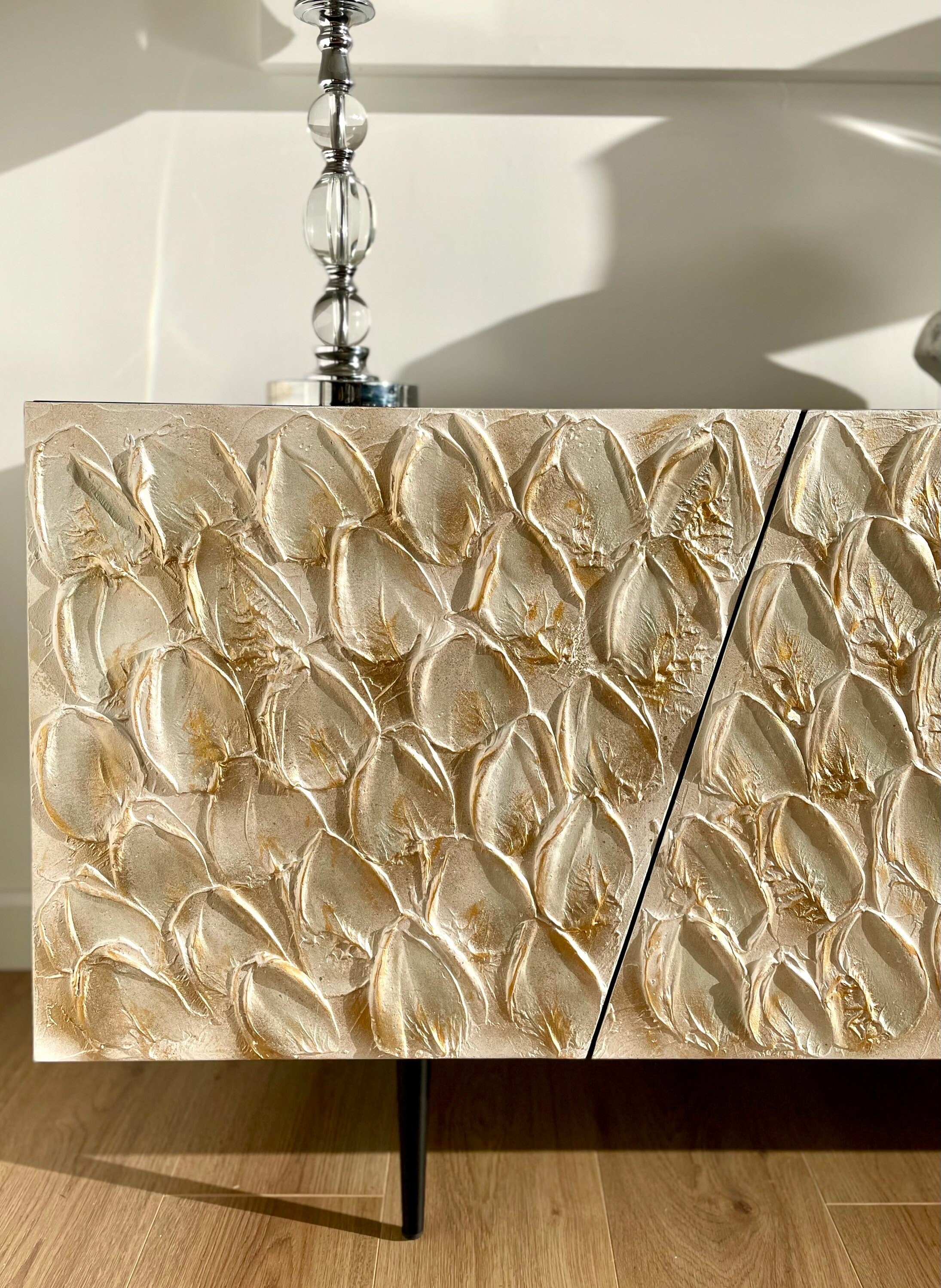 Close-up of a bespoke cabinet with a golden floral pattern on a wood floor.
