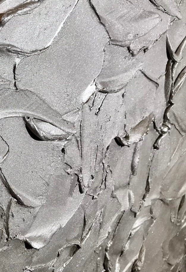 Close-up of a textured surface on a custom-made sideboard, with thick layers of gray, metallic paint applied in rough, sweeping strokes. The surface is shiny
