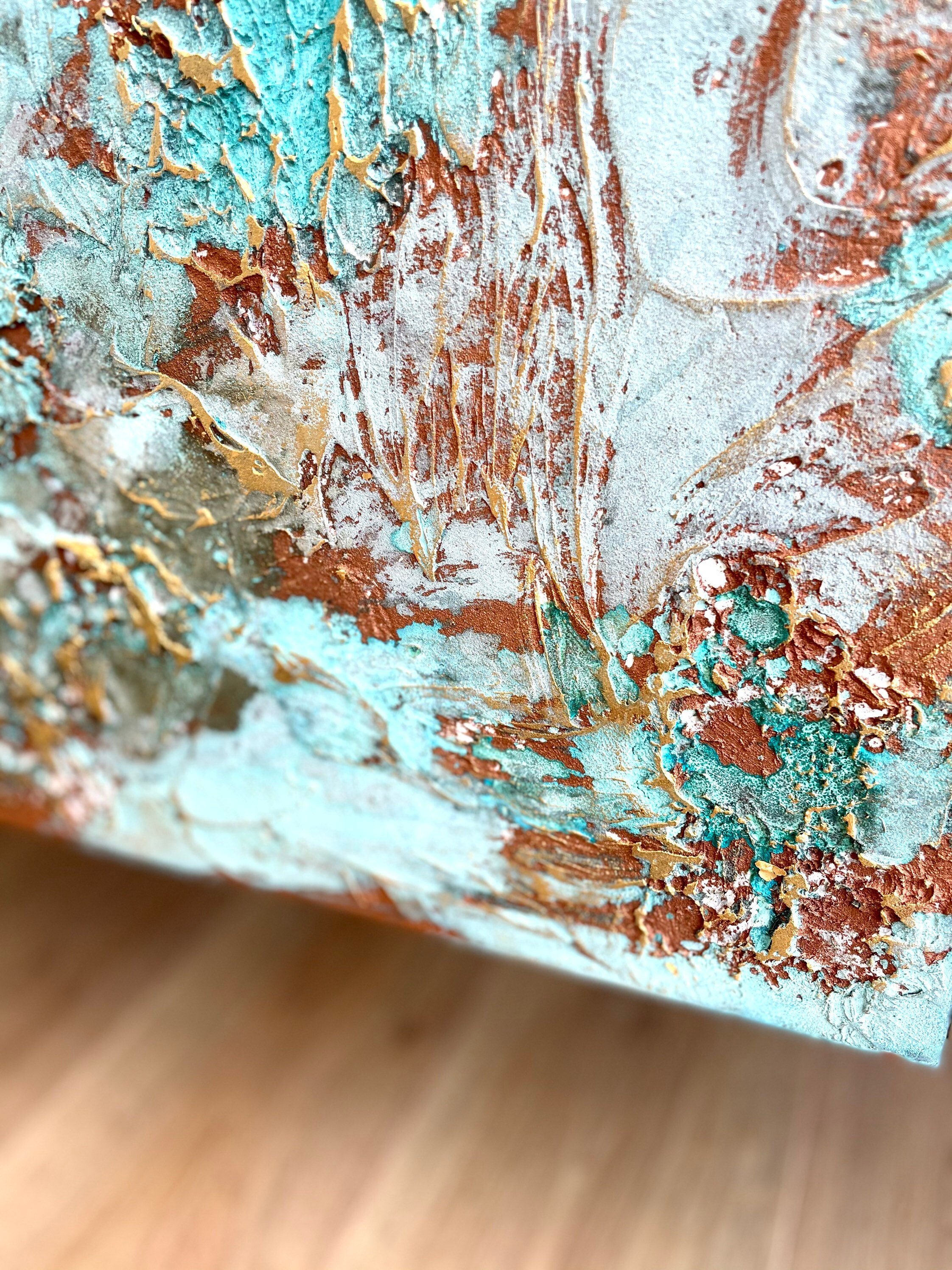Close-up of a textured abstract painting featuring swirls and patches of turquoise, copper, gold, and white.