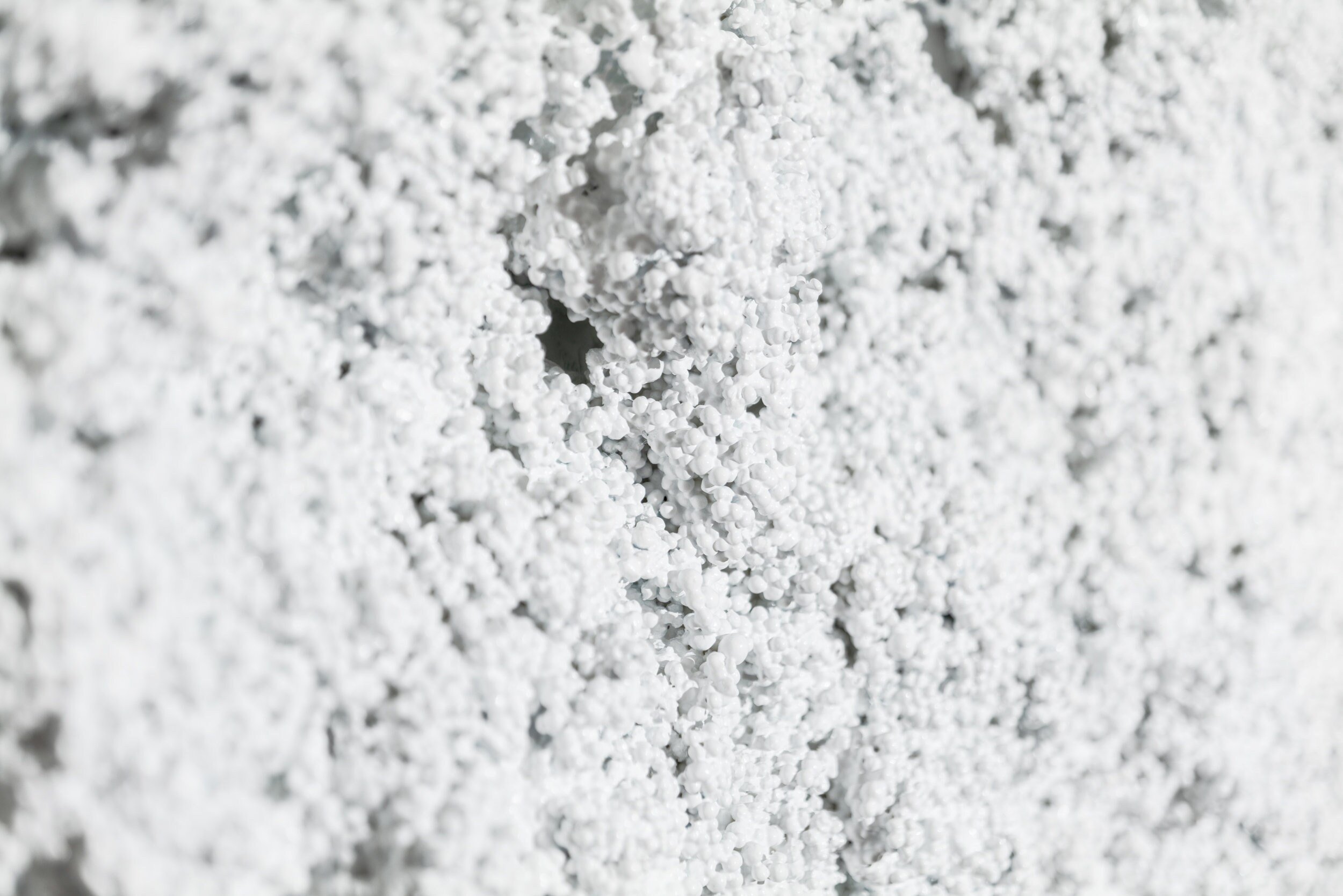 Close-up of a textured white surface with small, clustered, round granules resembling snow or foam. The texture creates a bumpy and uneven appearance across the image.
