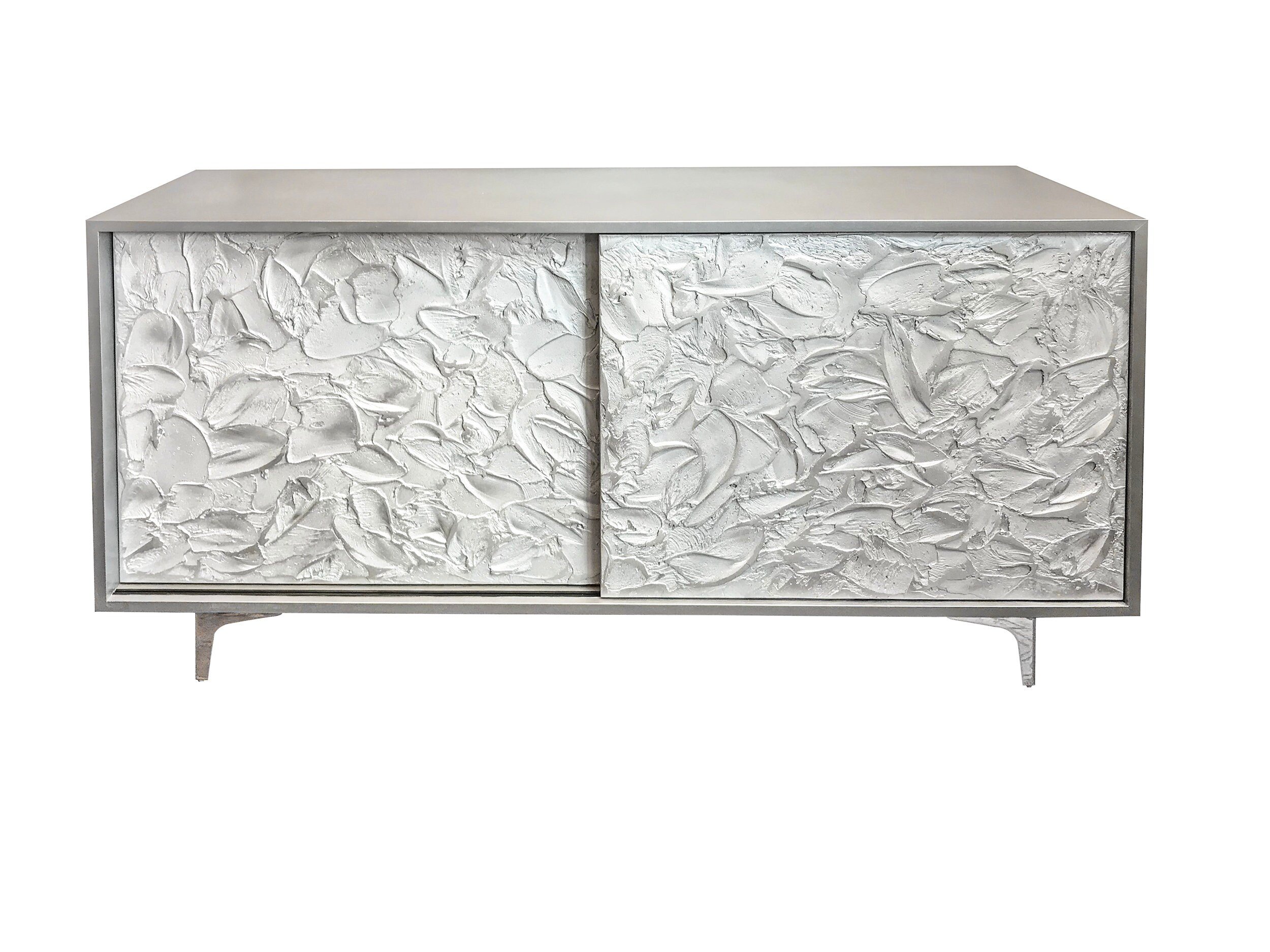 A modern sideboard with a smooth surface and two sliding doors, each showcasing textured art with an abstract, leaf-like pattern. The piece stands on slender, angled metal legs.