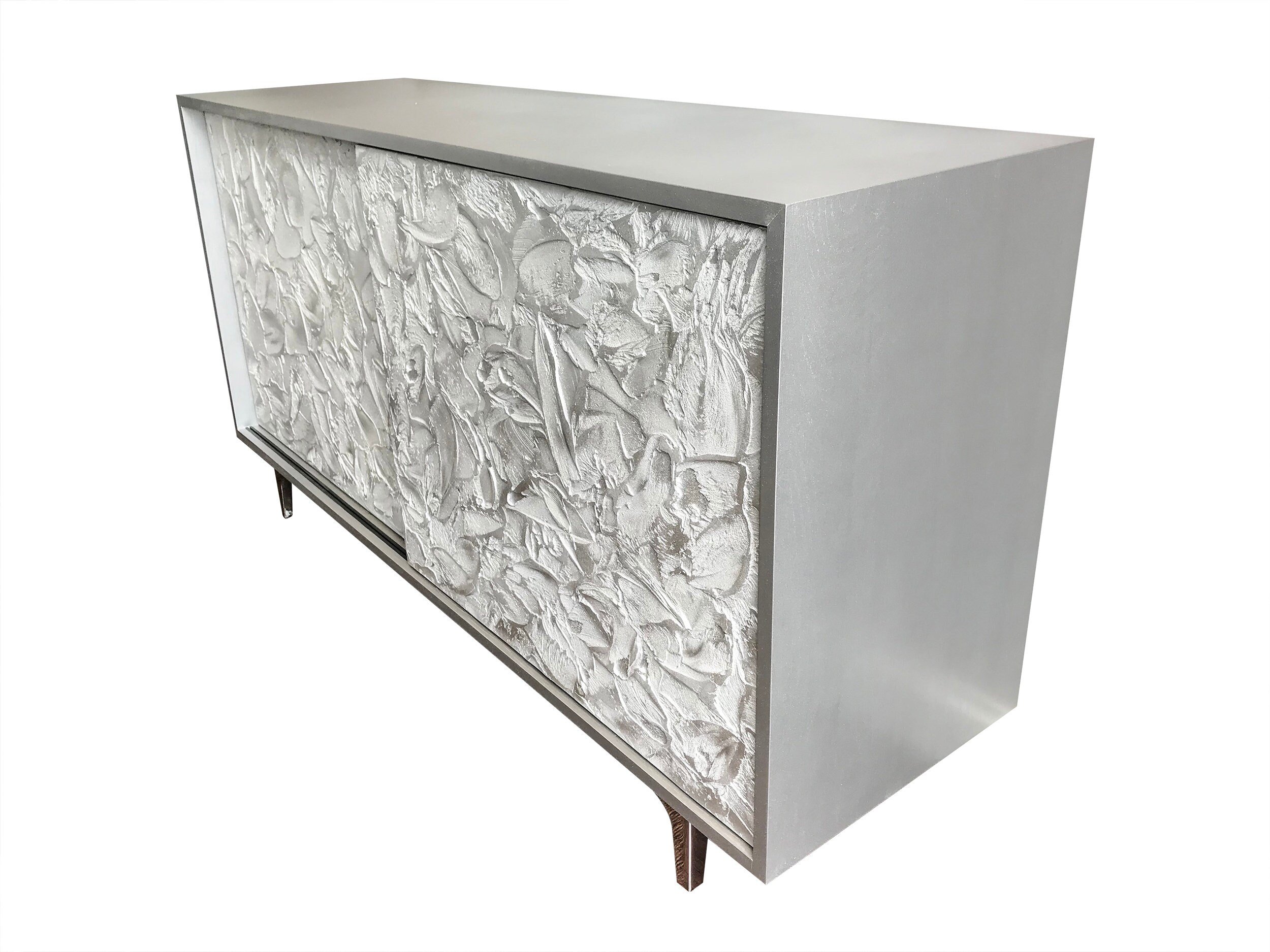A sleek rectangular cabinet with a textured floral pattern on the front panel and smooth, silver-gray surfaces. This custom-made sideboard stands on short legs, showcasing a modern, minimalist design.